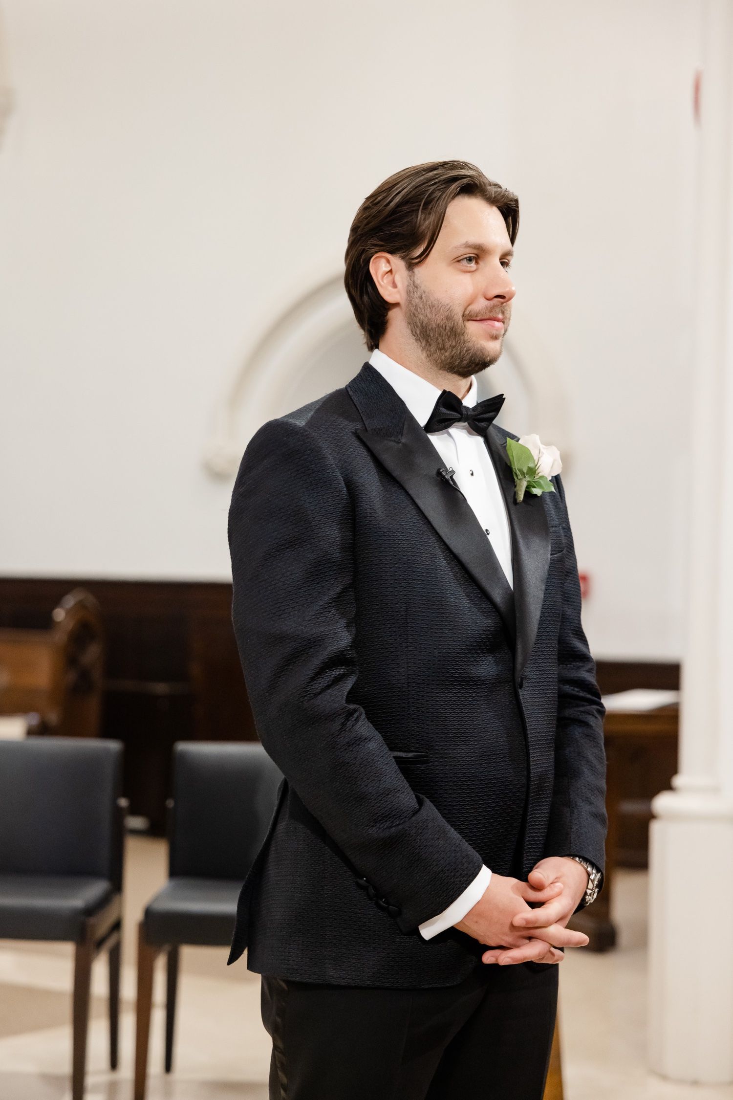 Formal portrait in church setting with classic black tuxedo and white boutonniere.