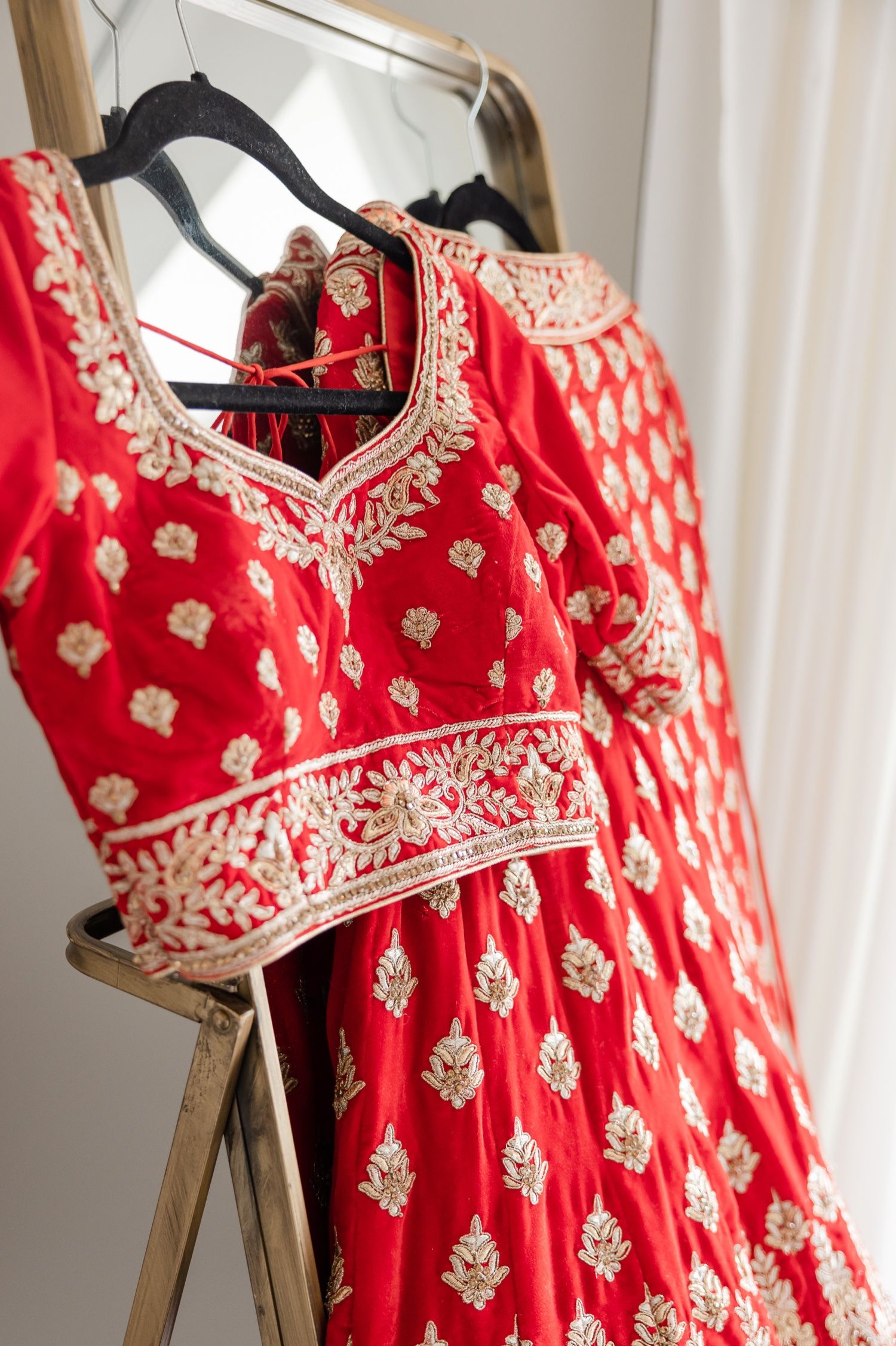 Traditional red Indian wedding dress with intricate gold embroidery hanging on display.