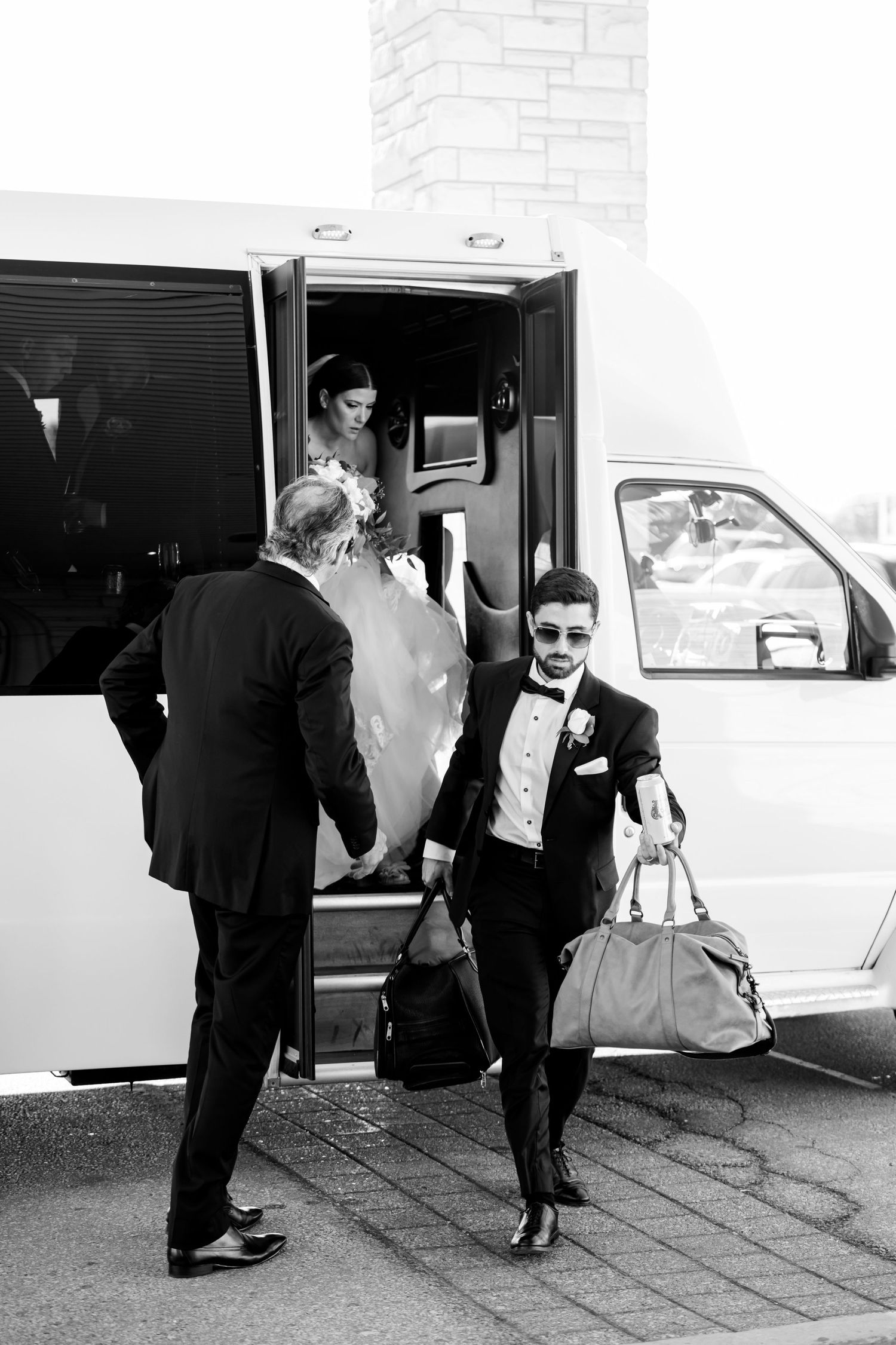 Black and white photo of wedding party members arriving at venue in formal attire.