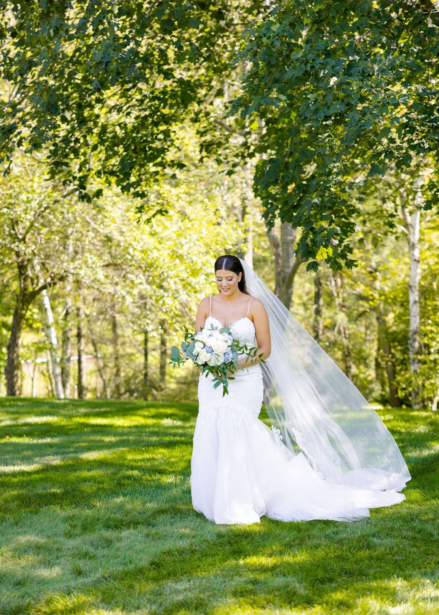 A beautiful wedding dress flows across green grass in a sunlit garden setting.