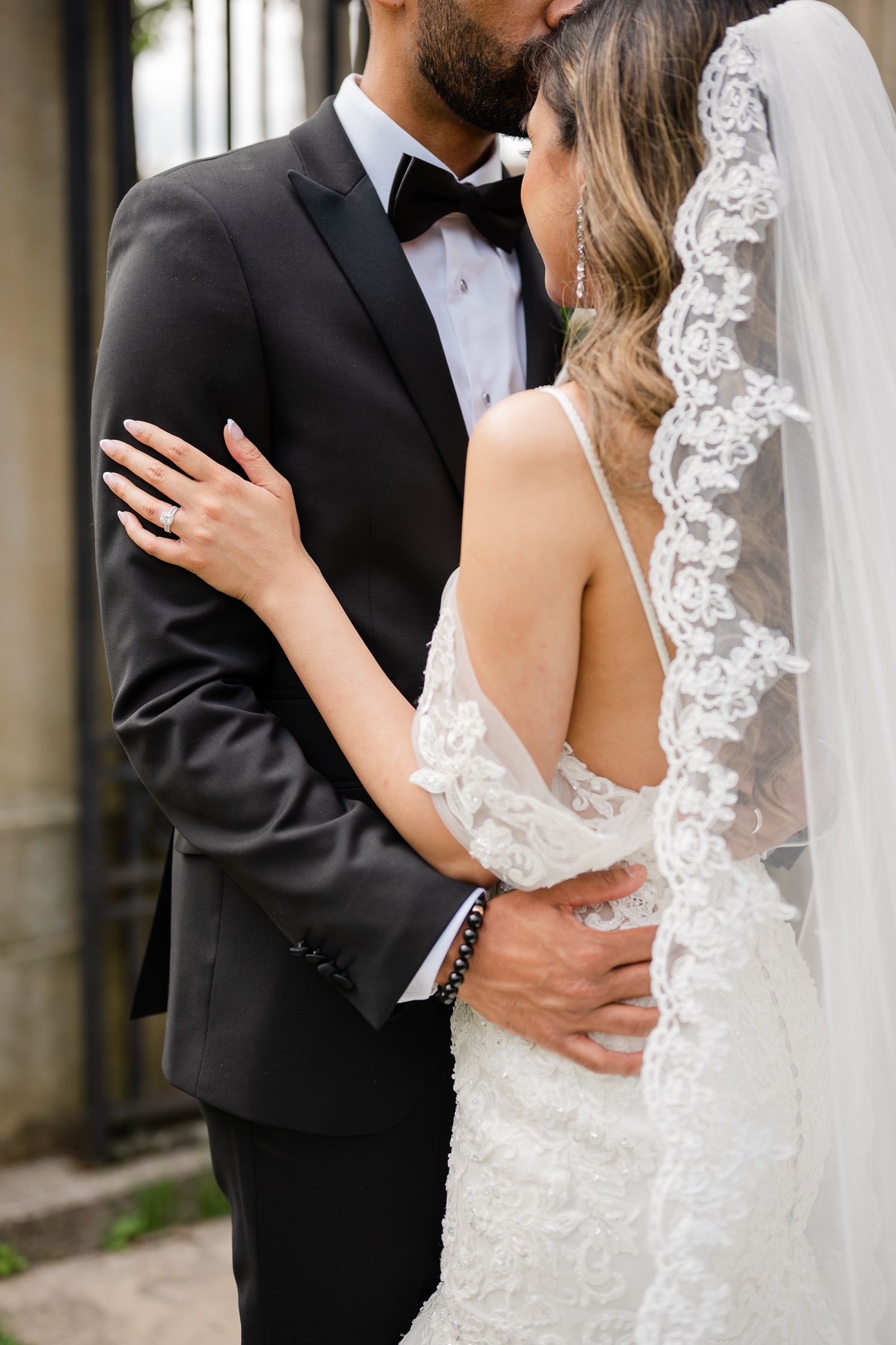 Close-up detail shot of newlyweds embracing, showing lace veil and formal wedding attire.