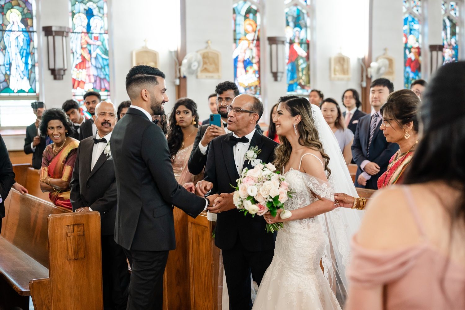 A wedding ceremony in progress inside a traditional church with wooden pews and stained glass windows.