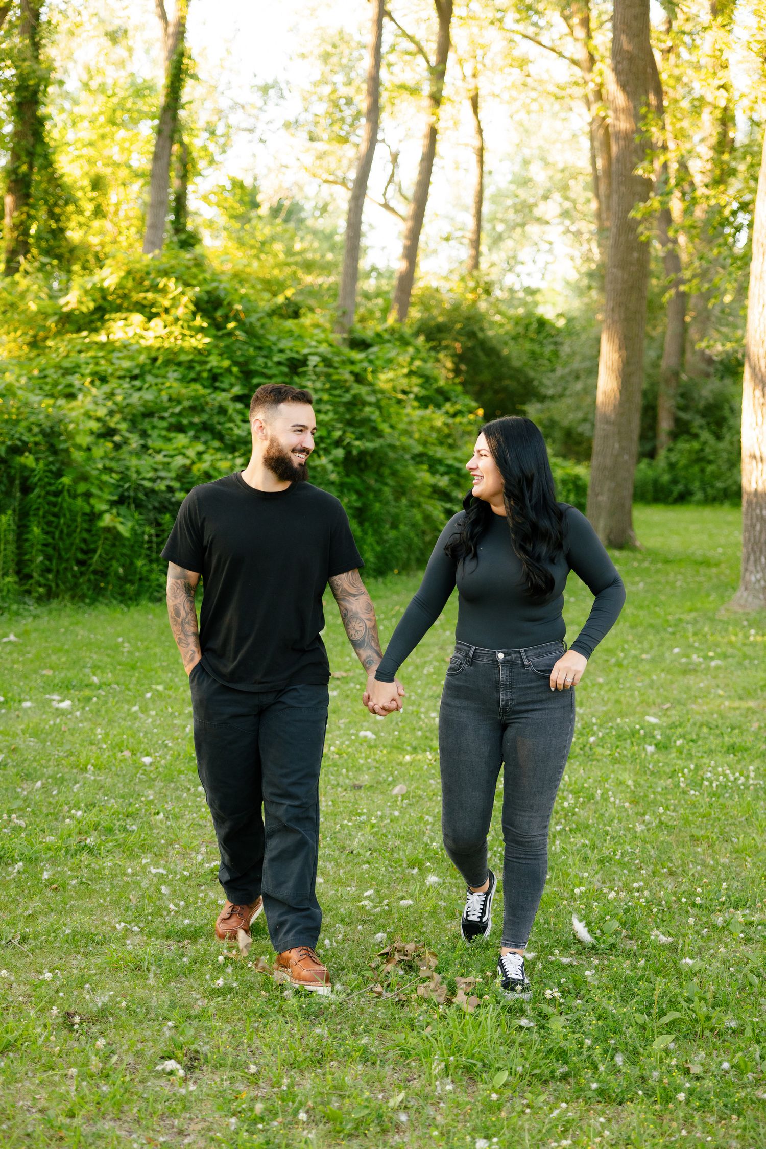 A couple walks hand in hand through a park with dappled sunlight filtering through the trees.