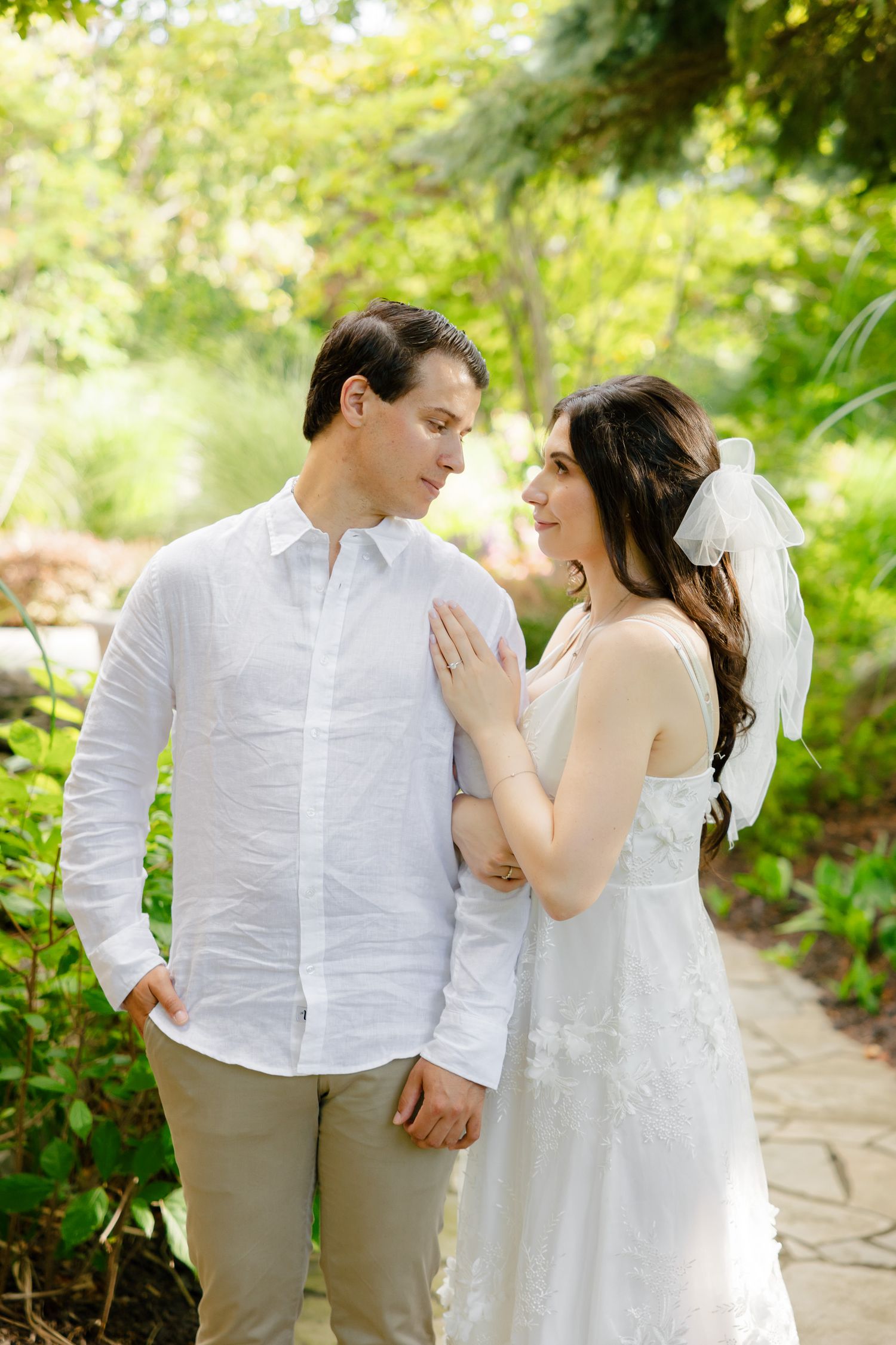 A couple shares an intimate moment in a garden setting wearing coordinated white outfits.