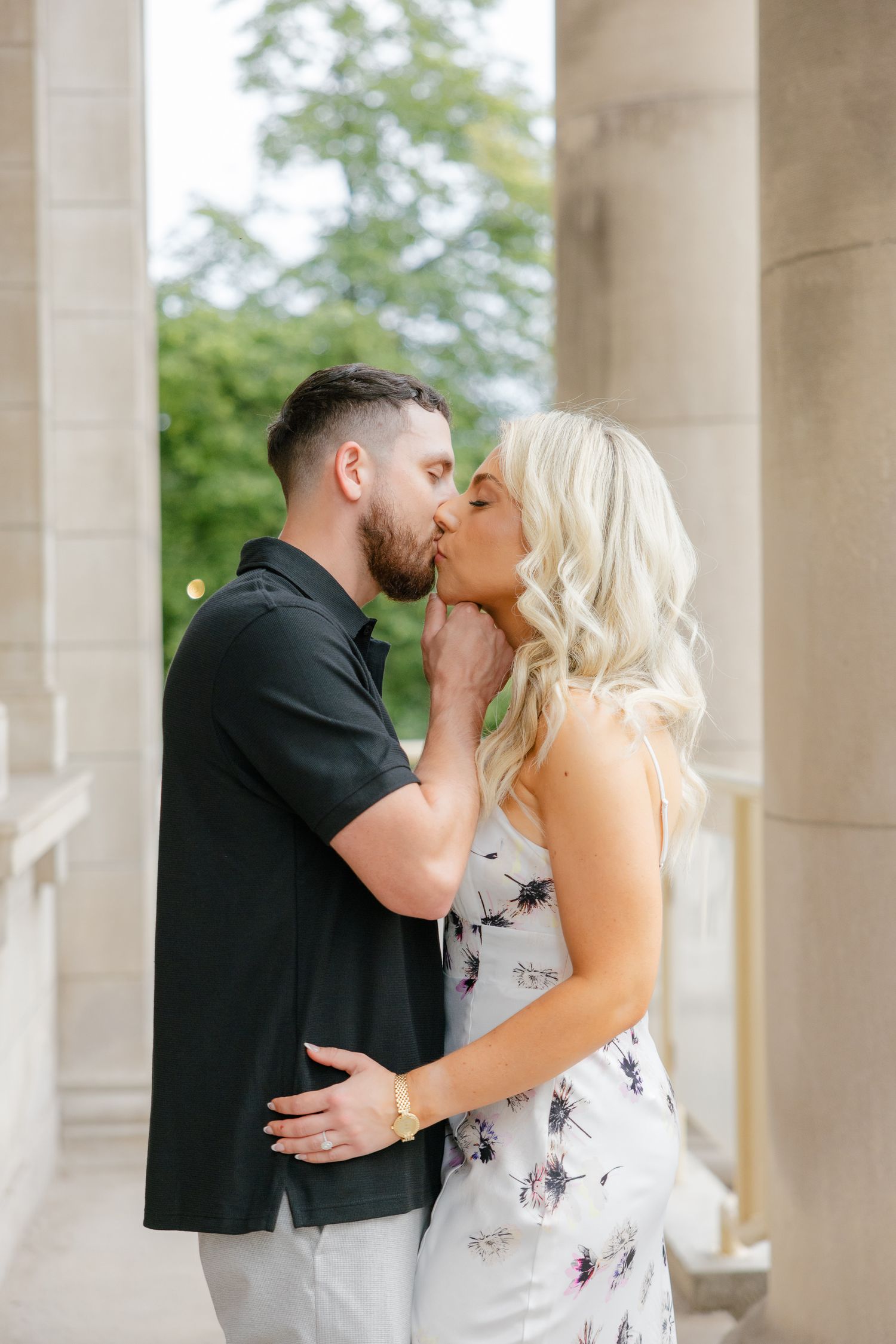 Intimate portrait of a couple kissing between ornate stone columns of a historic building.