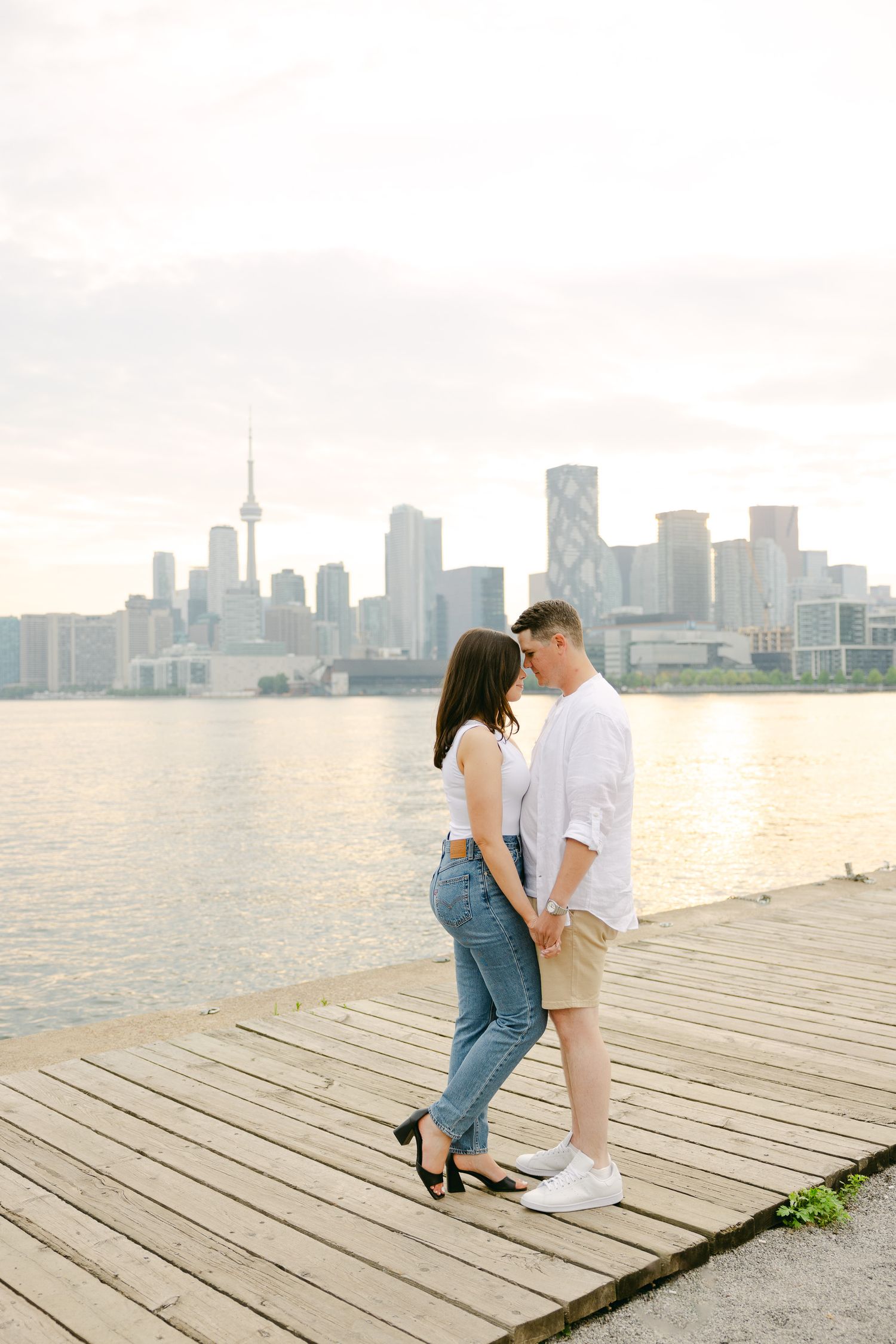 Romantic moment on wooden pier with Toronto's waterfront cityscape in background.