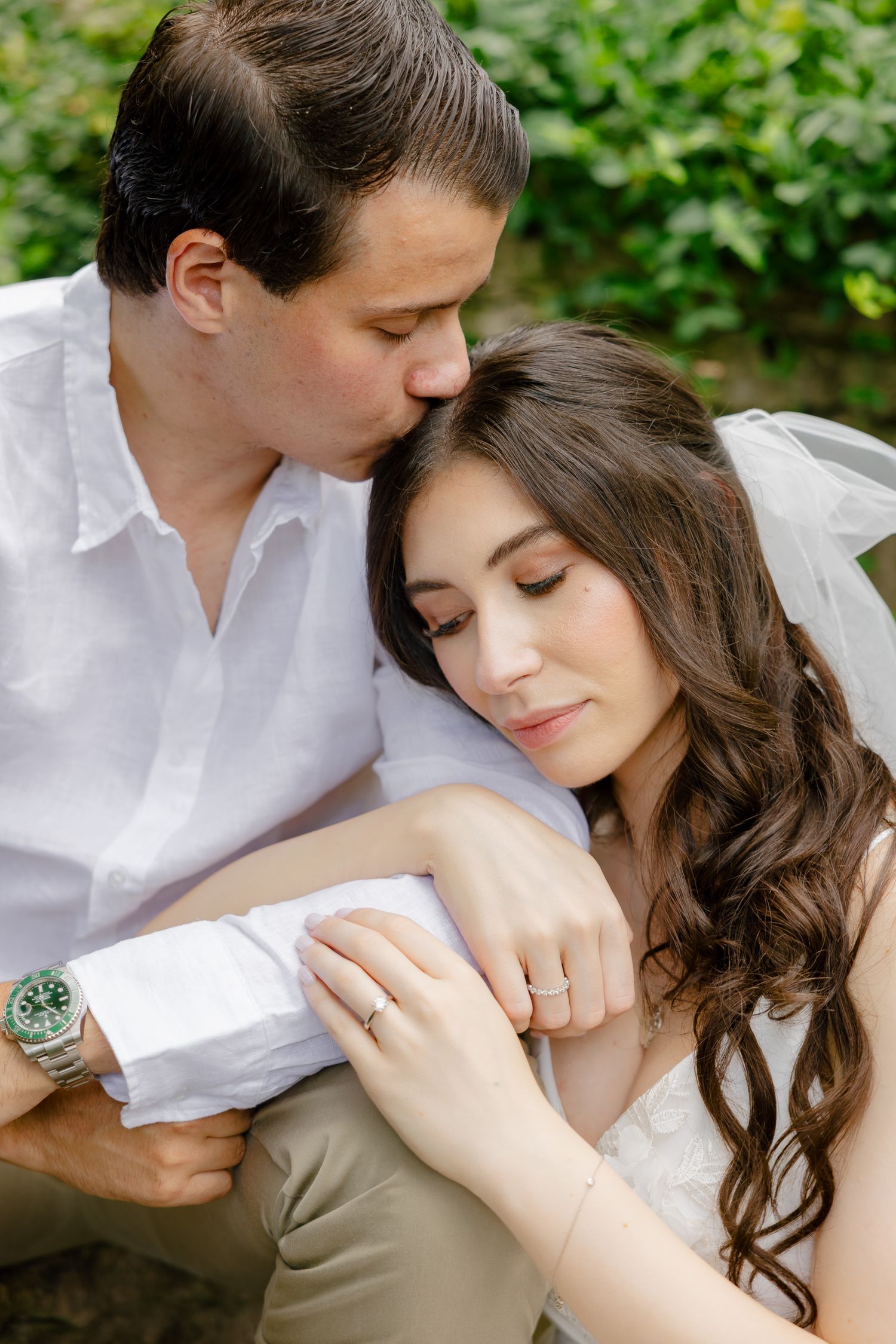 Romantic wedding couple in white attire sharing a close moment in a garden setting.