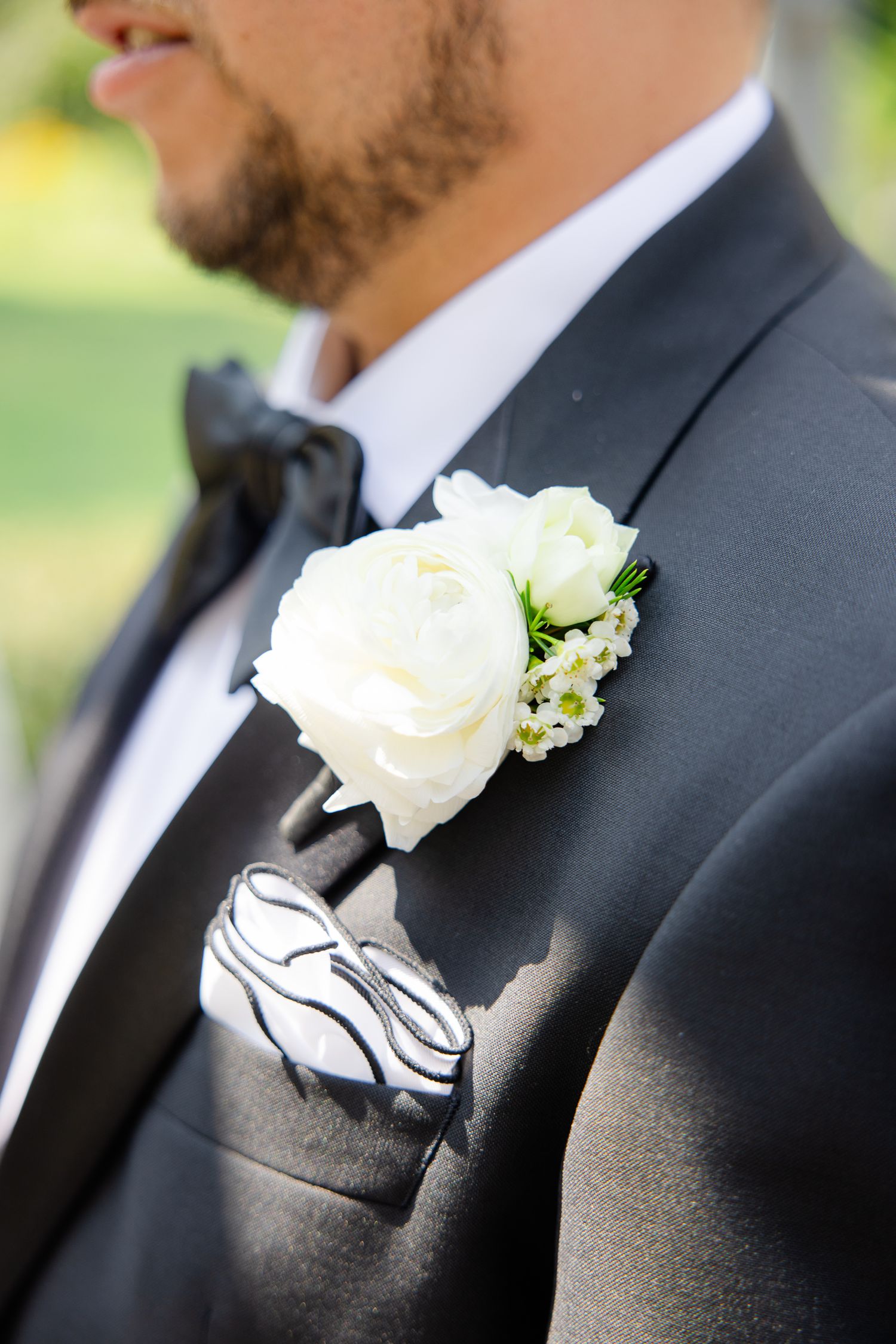 Close-up of white rose boutonniere on classic black tuxedo lapel.