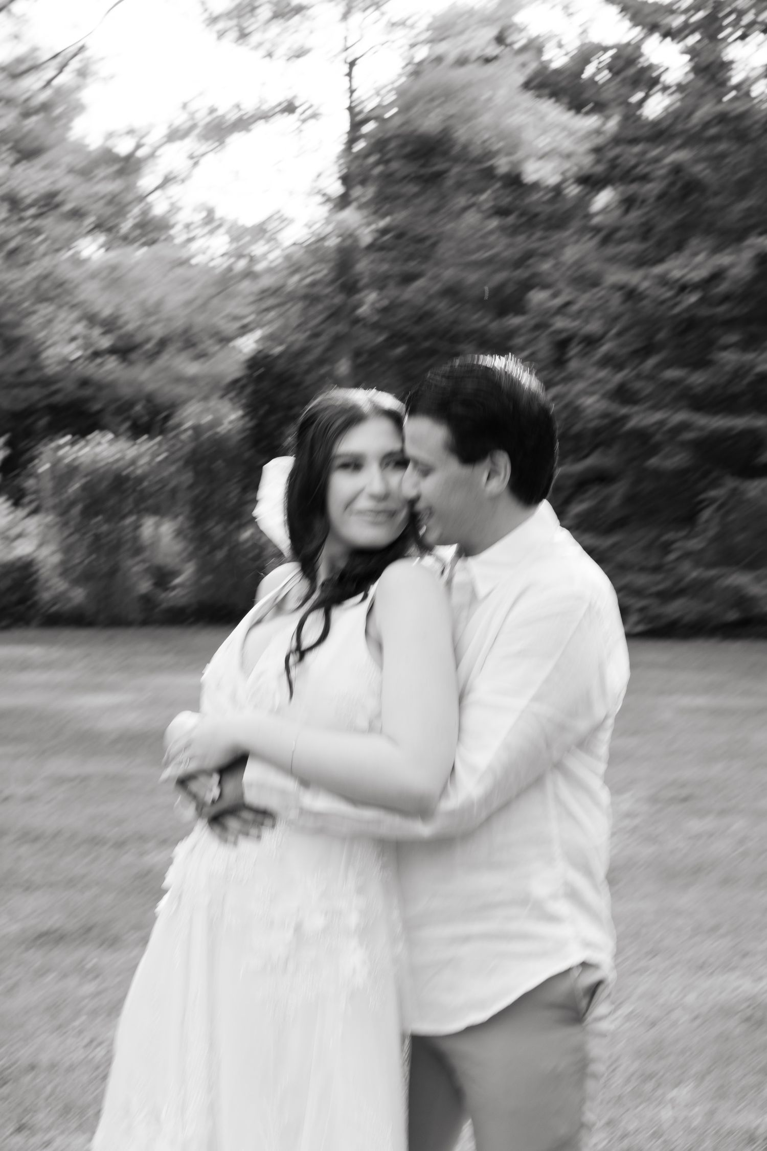 Black and white candid photo showing couple in intimate embrace outdoors.