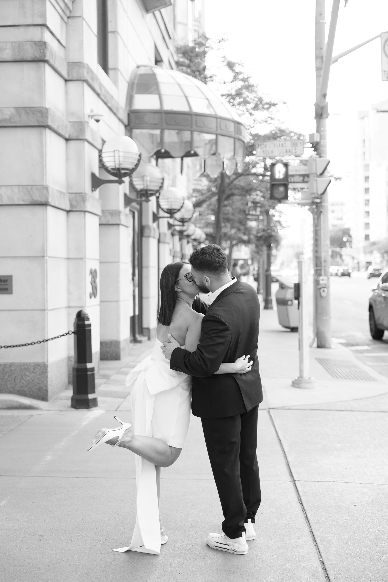 A romantic moment captured between a couple on a city sidewalk with decorative street lamps.