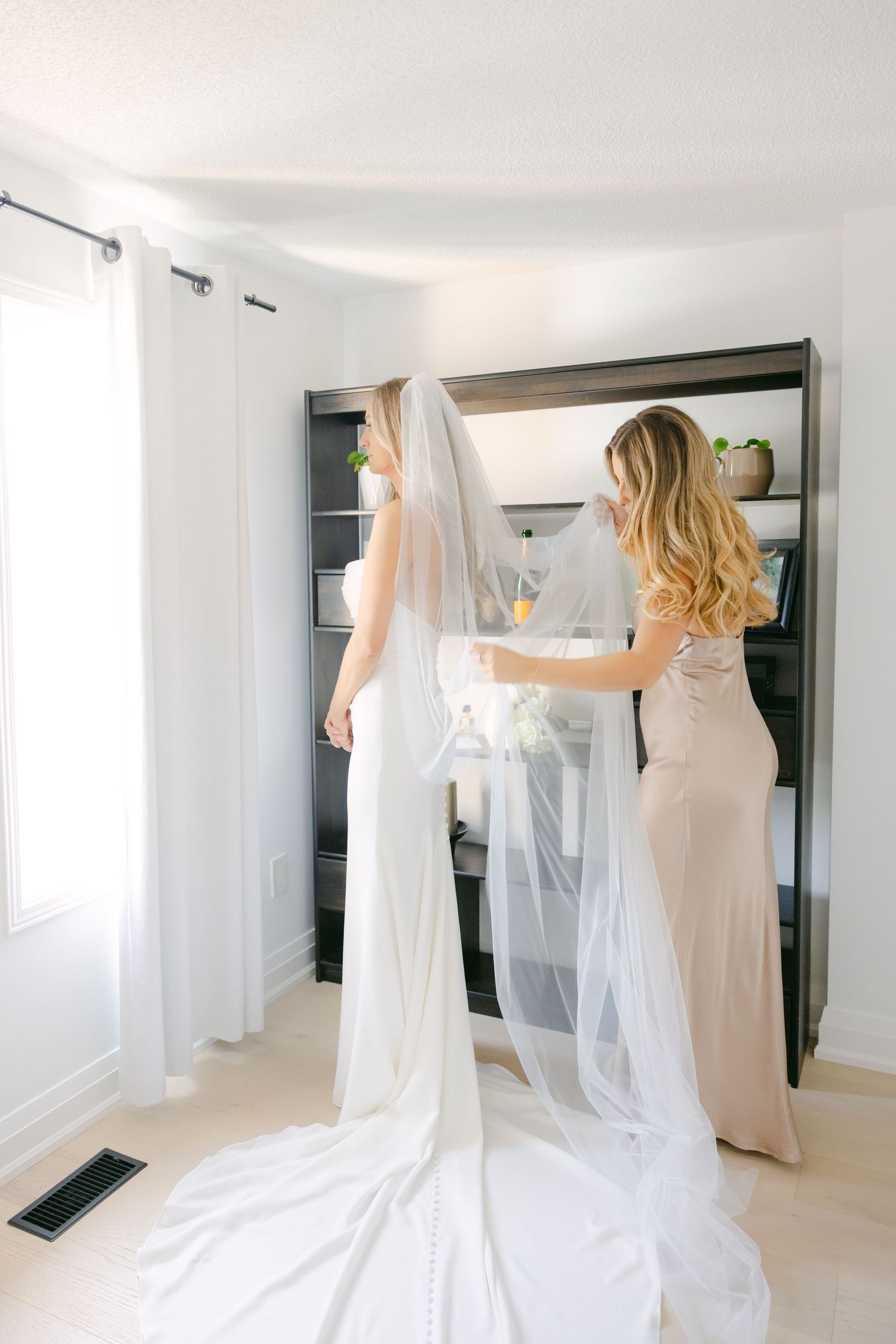 A flowing white wedding veil is being arranged in a bright room with dark shelves.