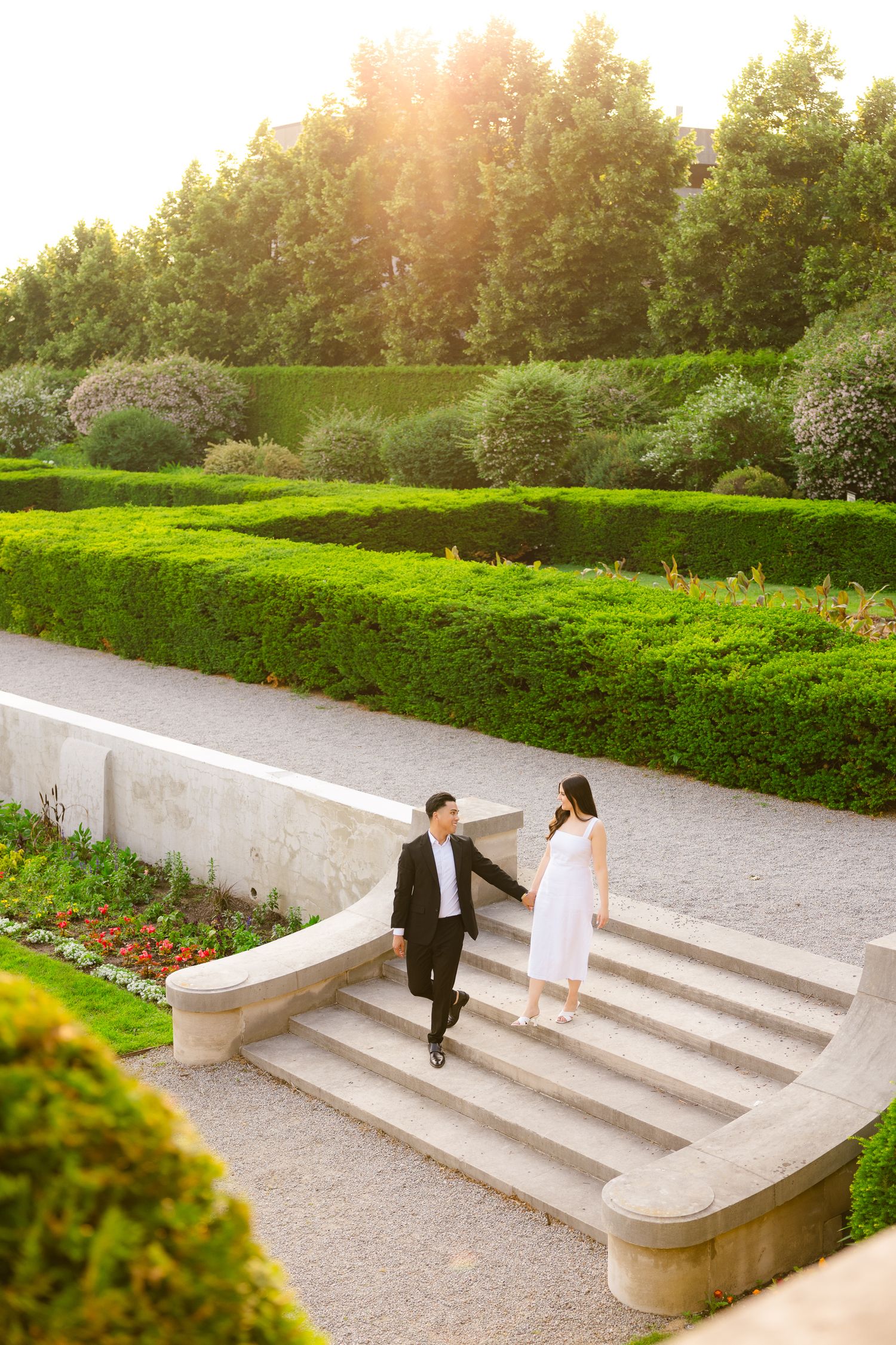 A couple stands on elegant stone steps surrounded by lush garden landscaping.