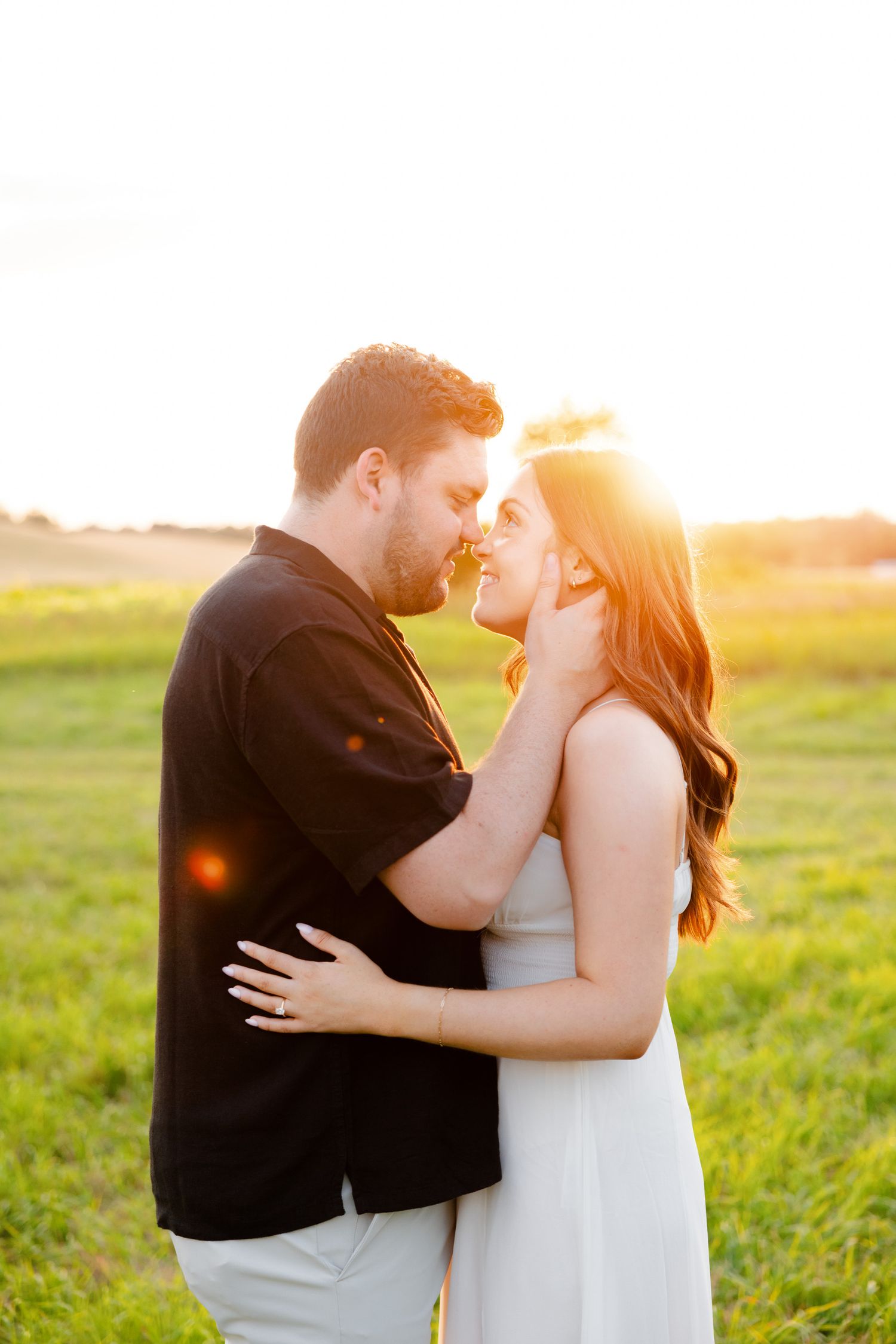 Romantic sunset portrait of couple in casual attire sharing intimate moment in field.