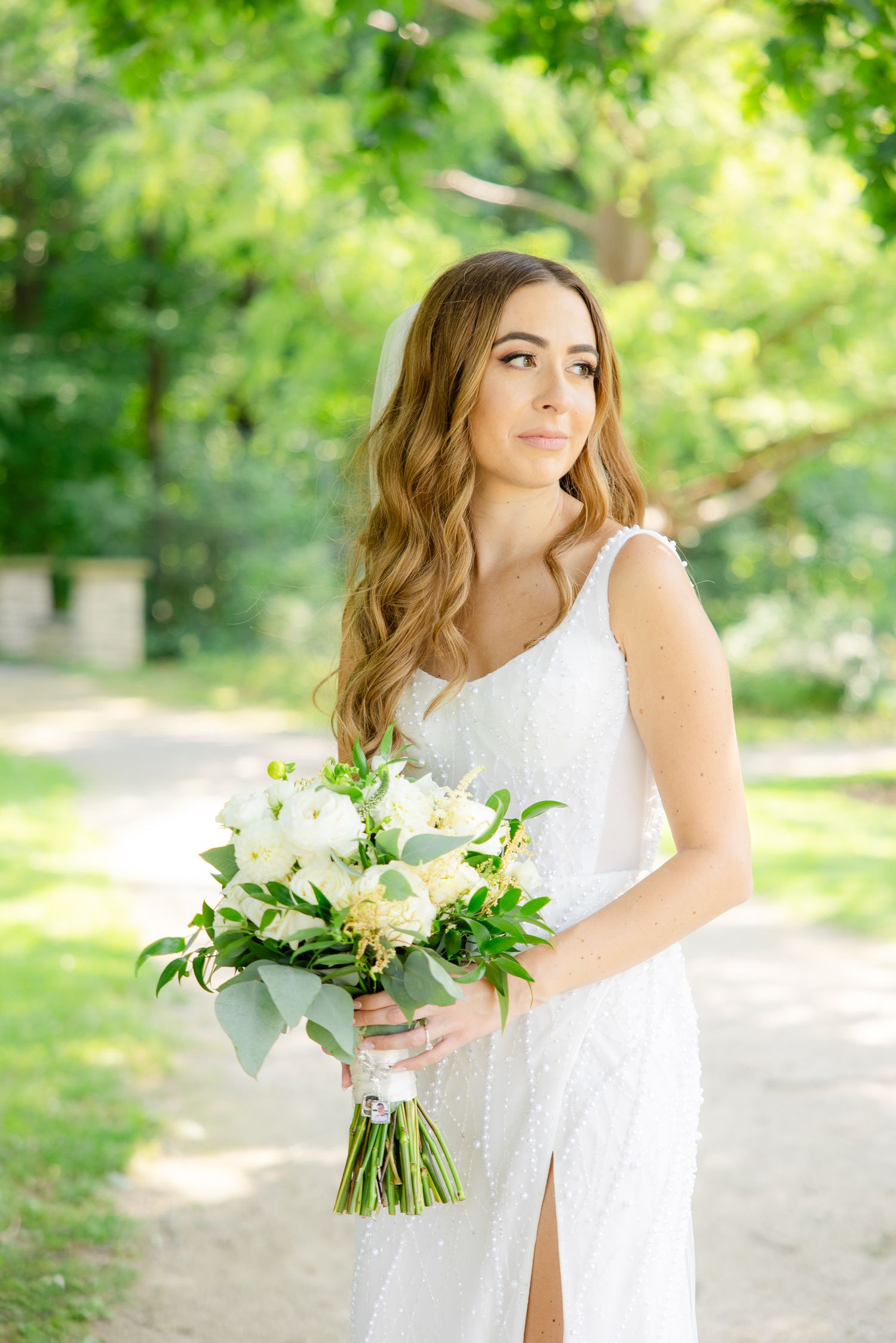 A bride in a sleek white gown holds a classic white and green bouquet outdoors.