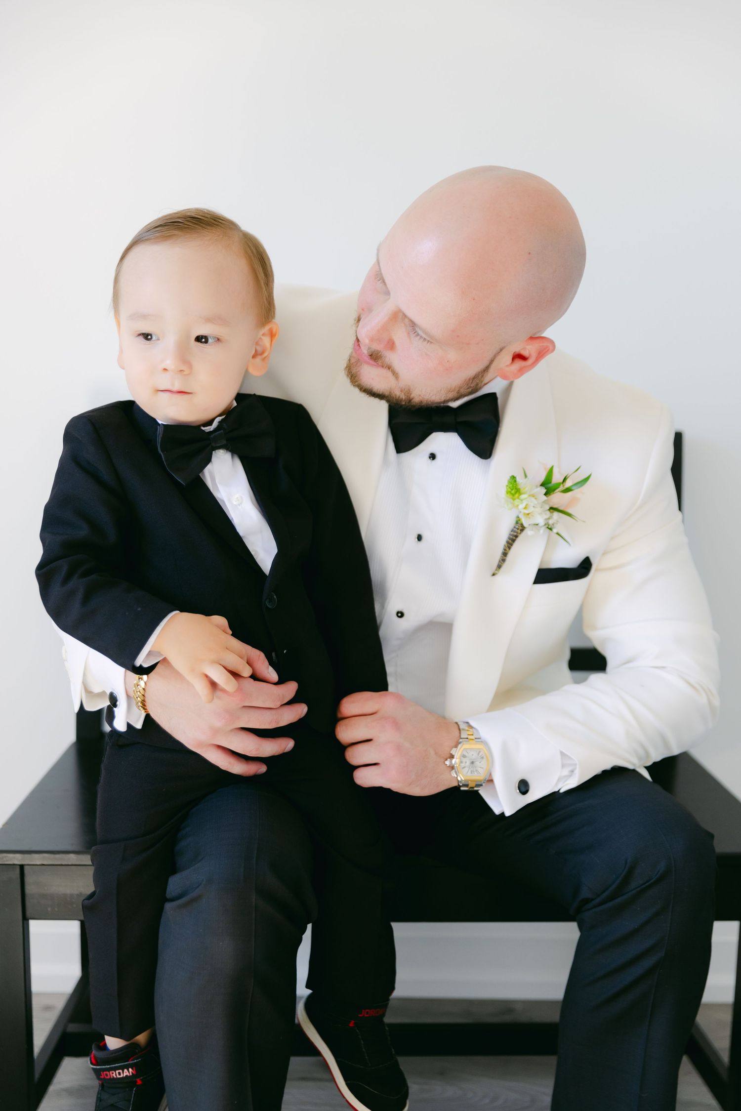 Two people in matching formal wear share a tender moment on a black bench.