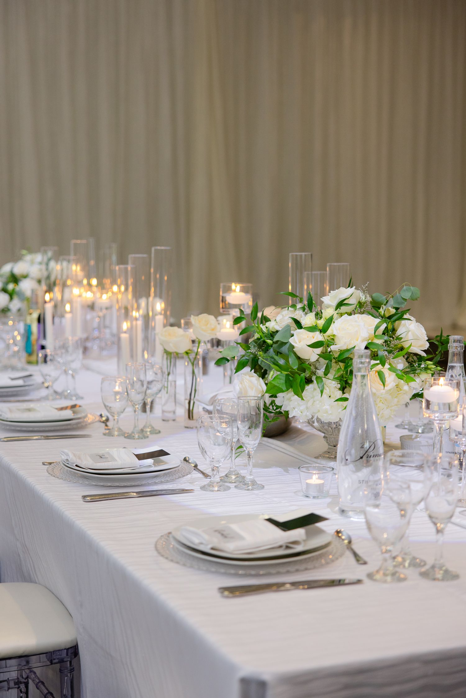 White tablescapes with fresh flowers and candles arranged for an upscale wedding reception.