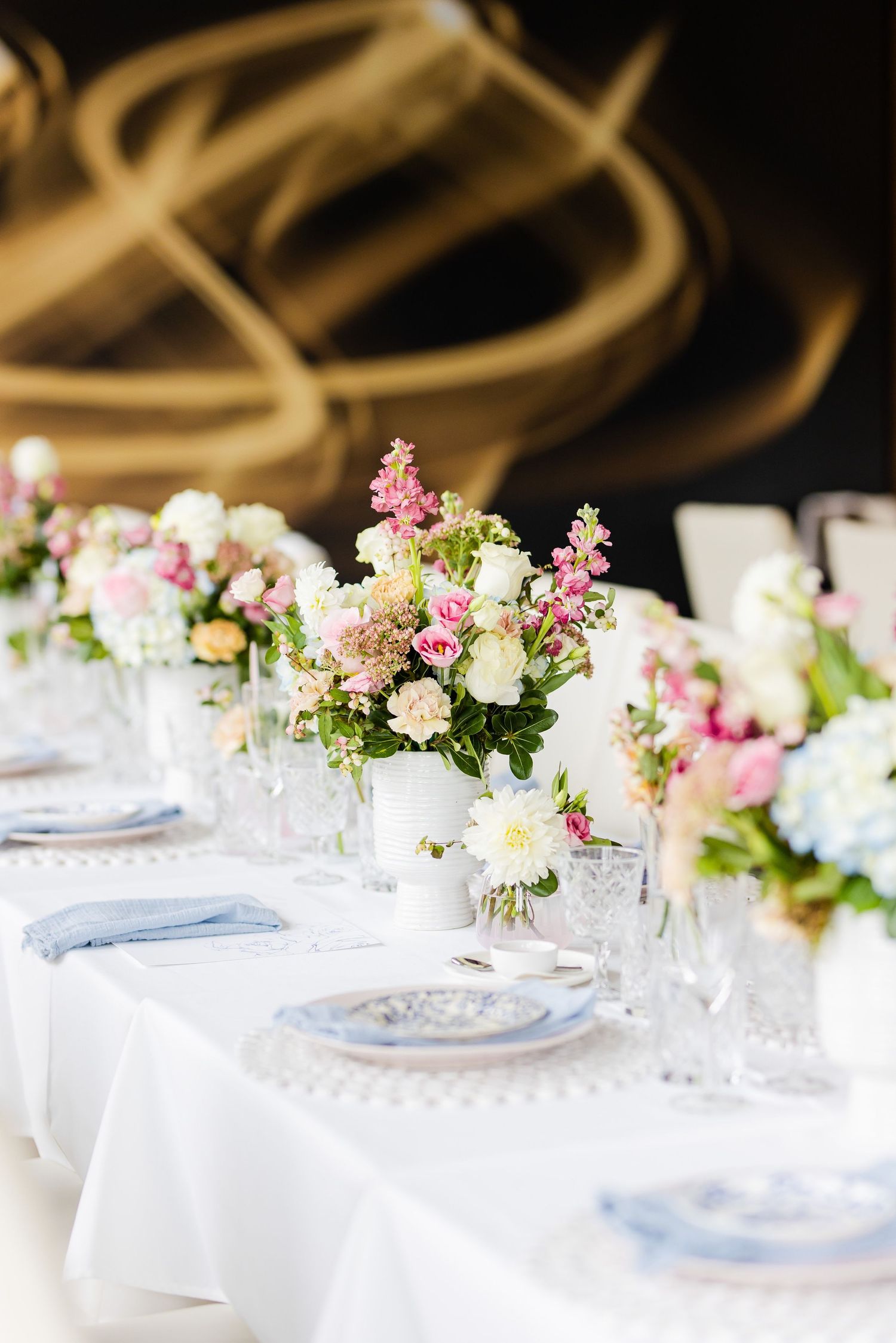 Elegant table setting with pink and white floral centerpieces in mason jars on crisp white linens.