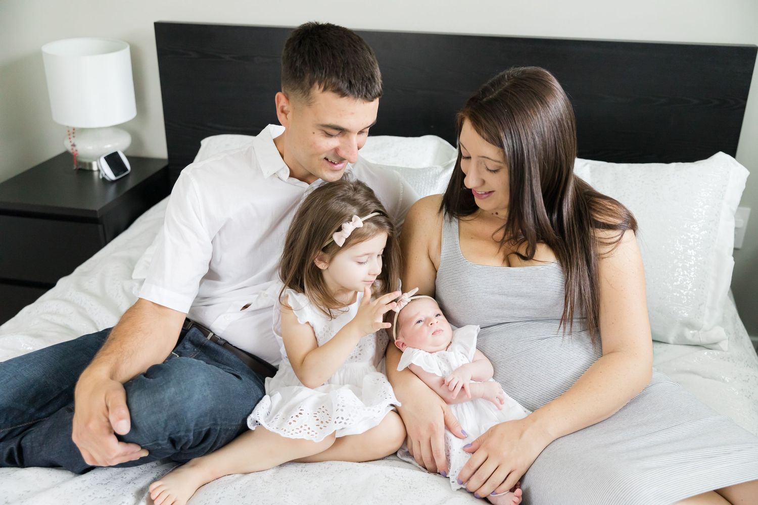 Family sitting together on bed with newborn baby in intimate lifestyle portrait.