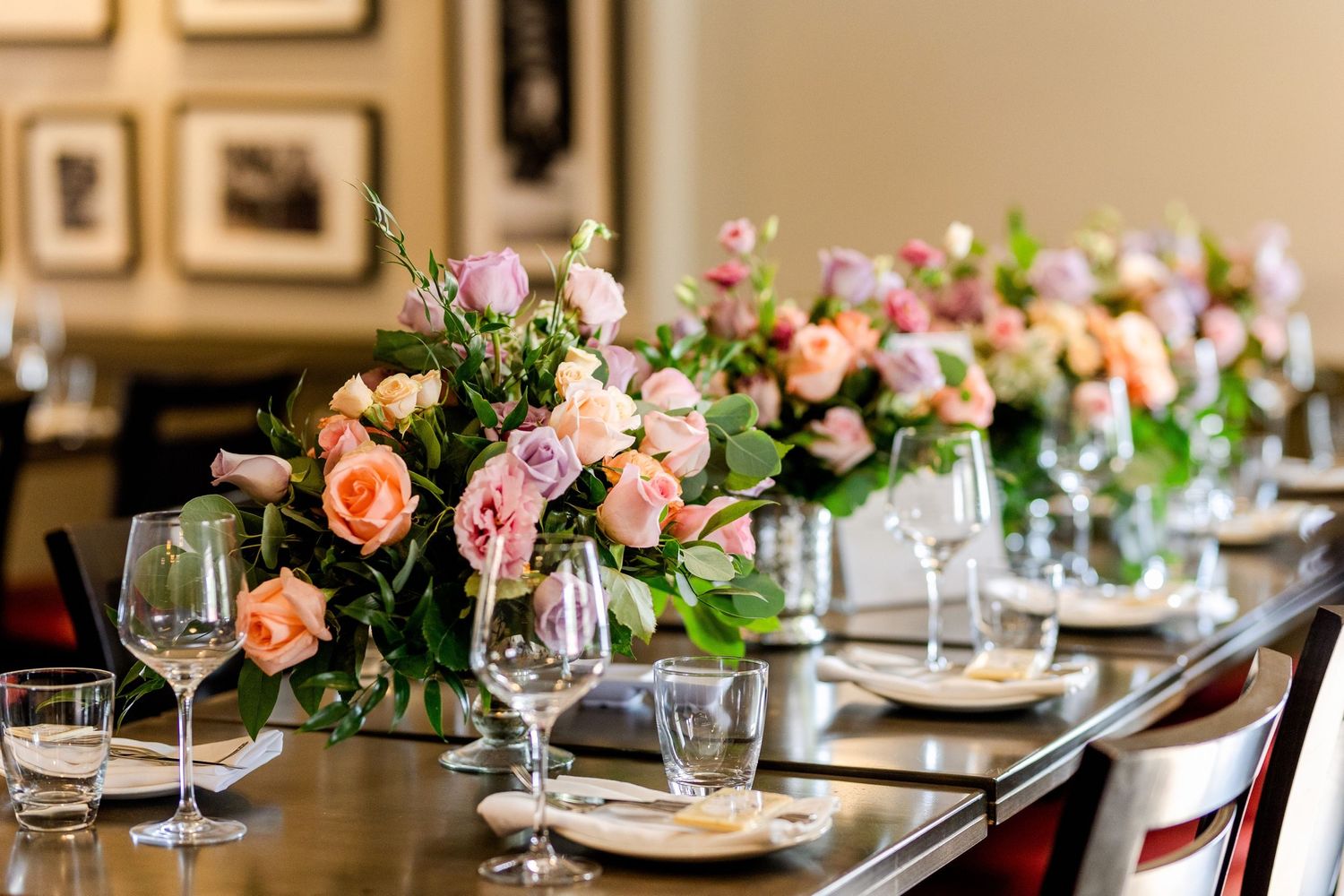 Formal dining table set with pink and peach floral arrangements and crystal stemware.