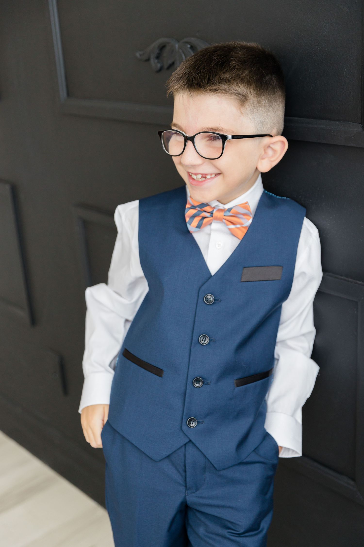 Stylish formal wear featuring a navy vest and coral bow tie with white shirt against dark wall.
