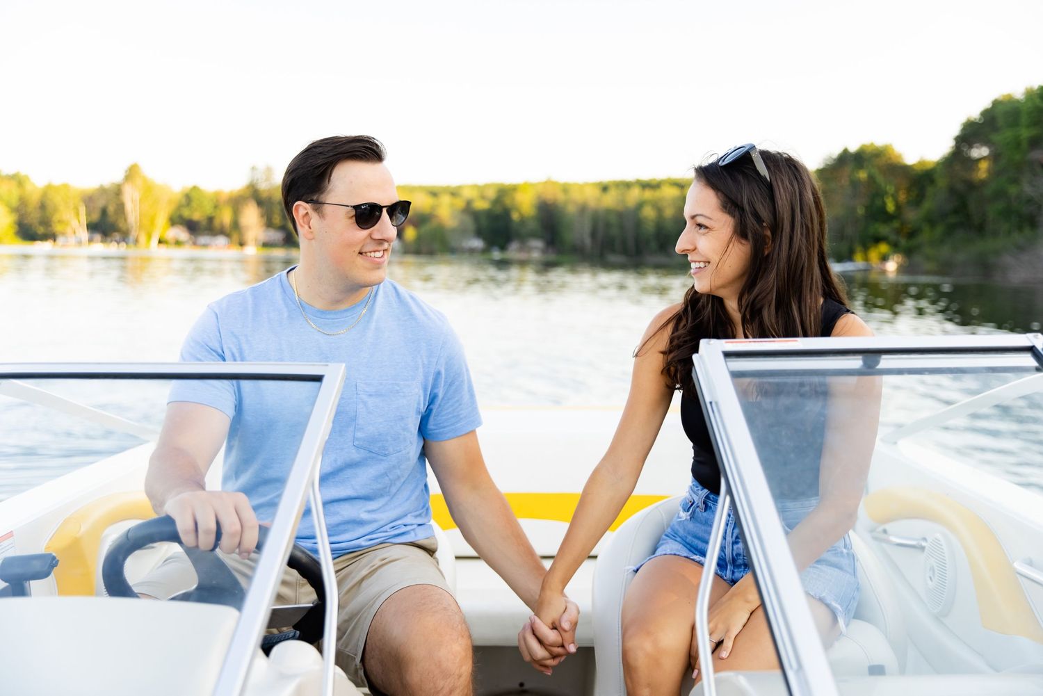 Couple holding hands while sitting in captain chairs on white speedboat.