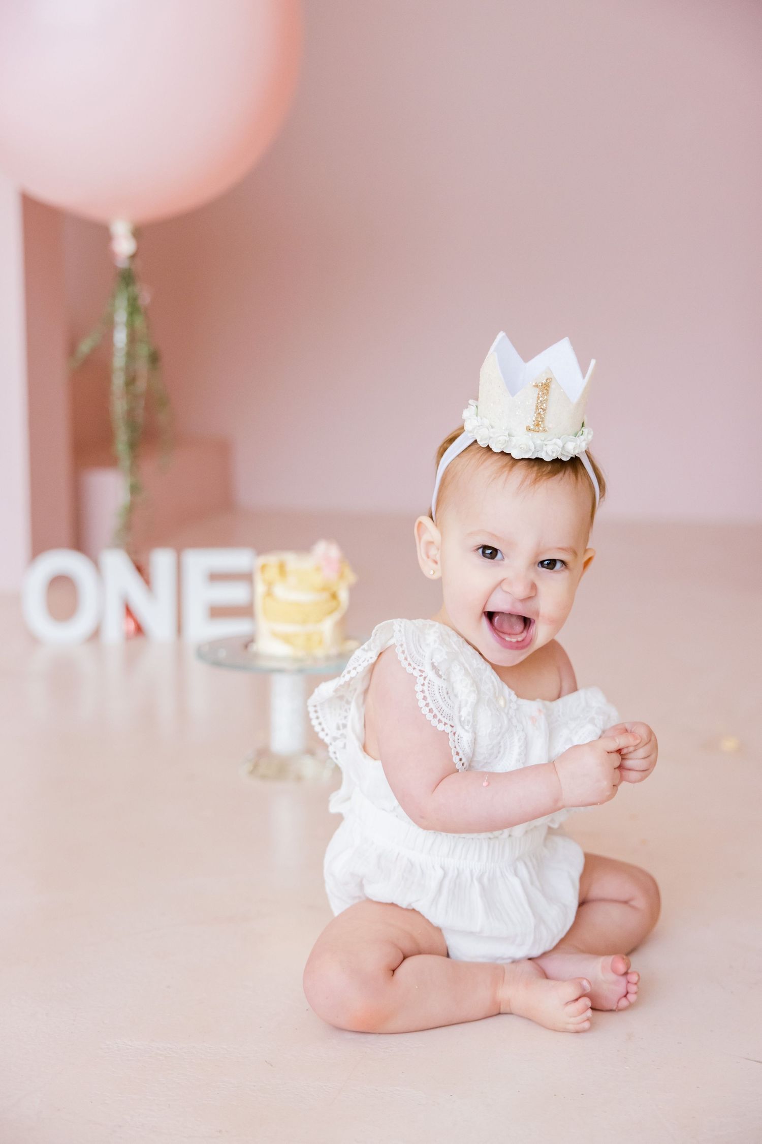 First birthday celebration setup with pink balloon, cake, and white decorative elements.