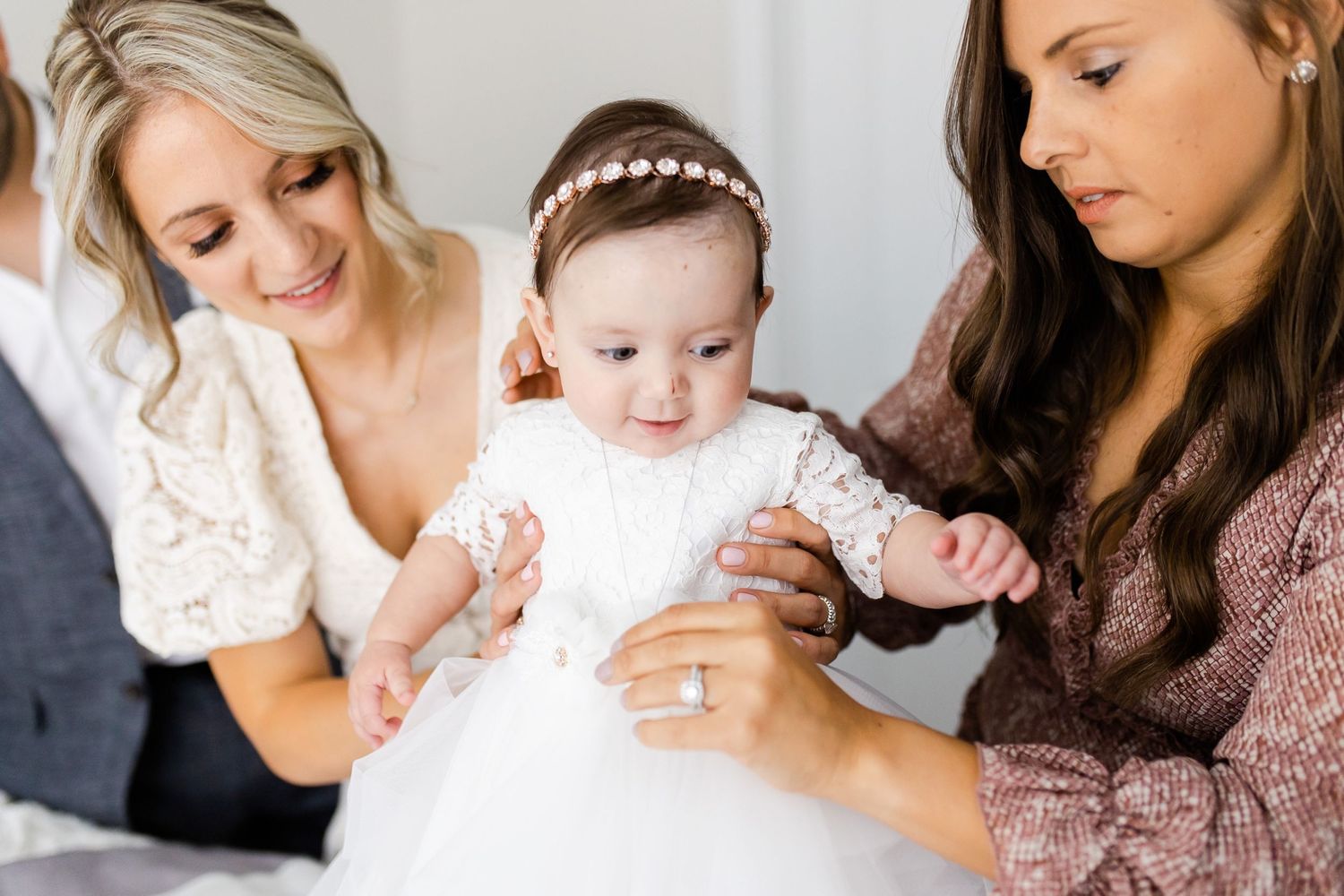 Group helping with baby in white dress during intimate family photo session.