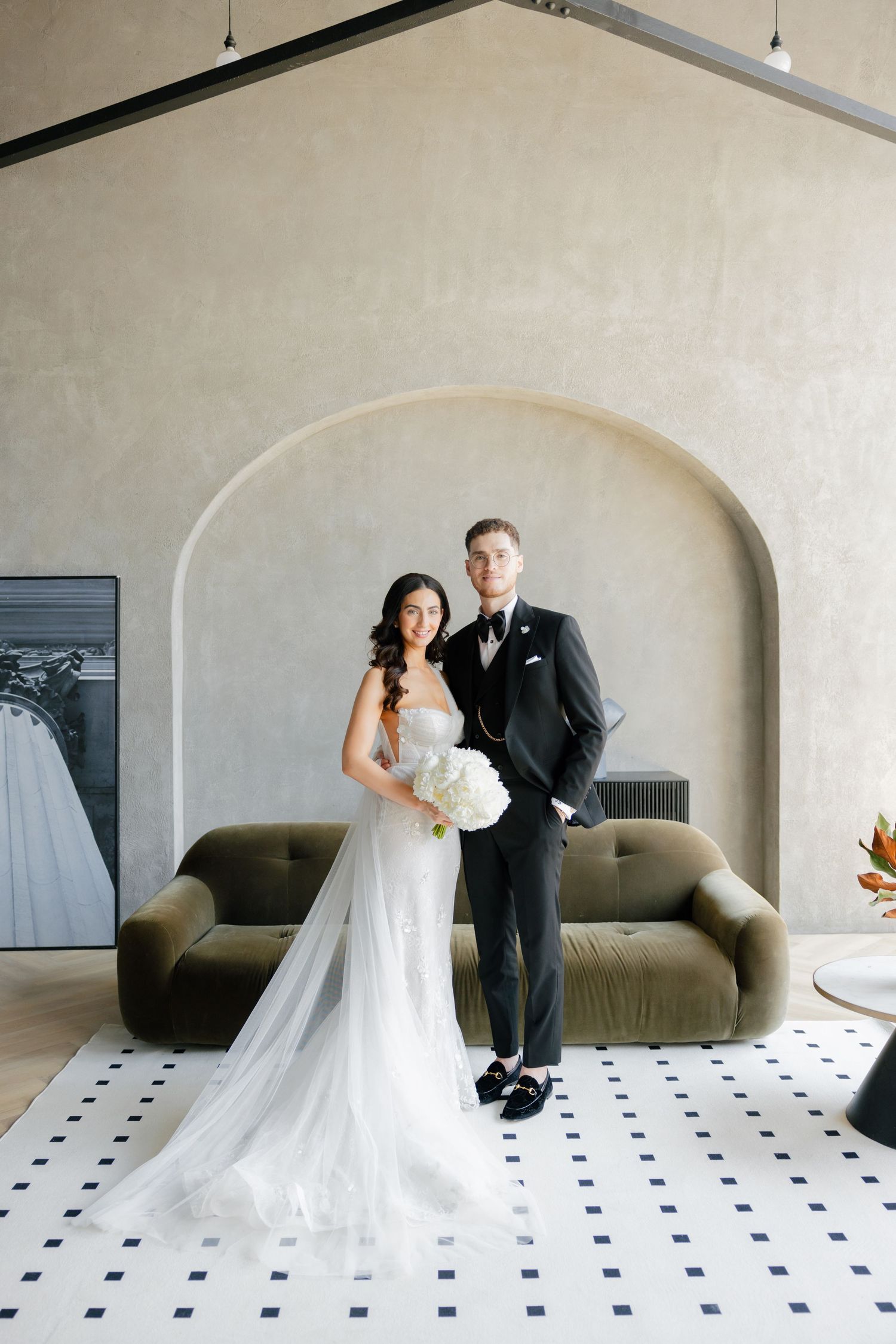 Elegant wedding portrait of couple standing in modern interior with arched wall and tiled floor.