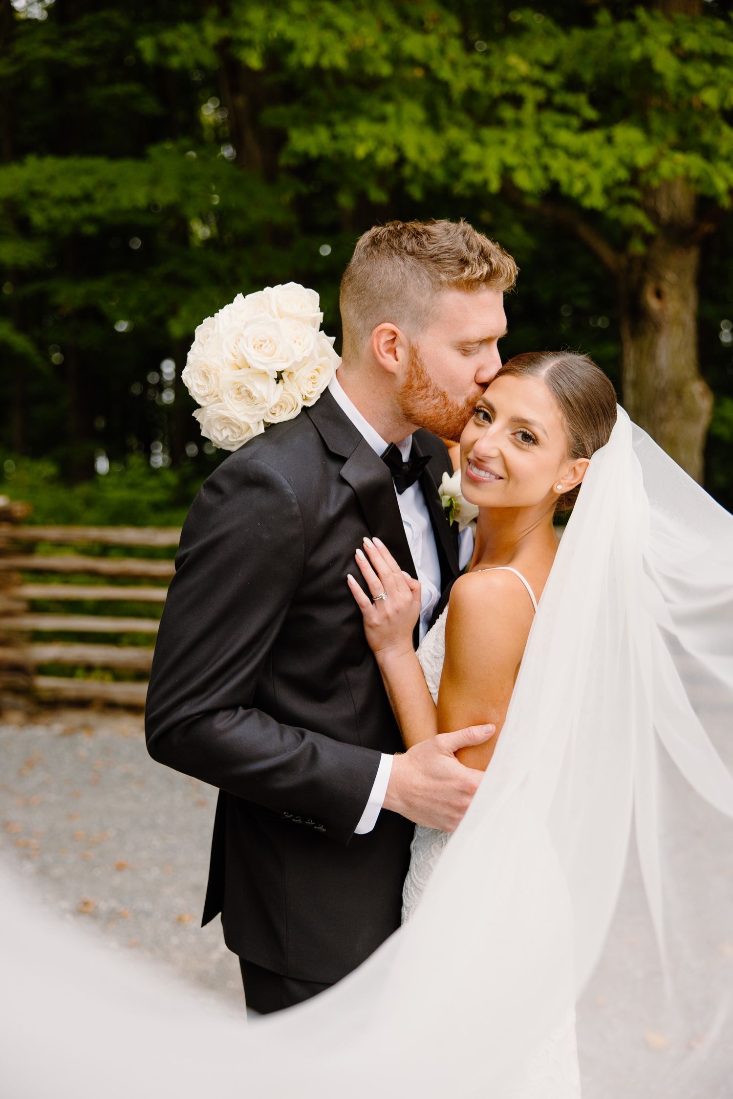Romantic wedding portrait with white floral bouquet against green forest backdrop.