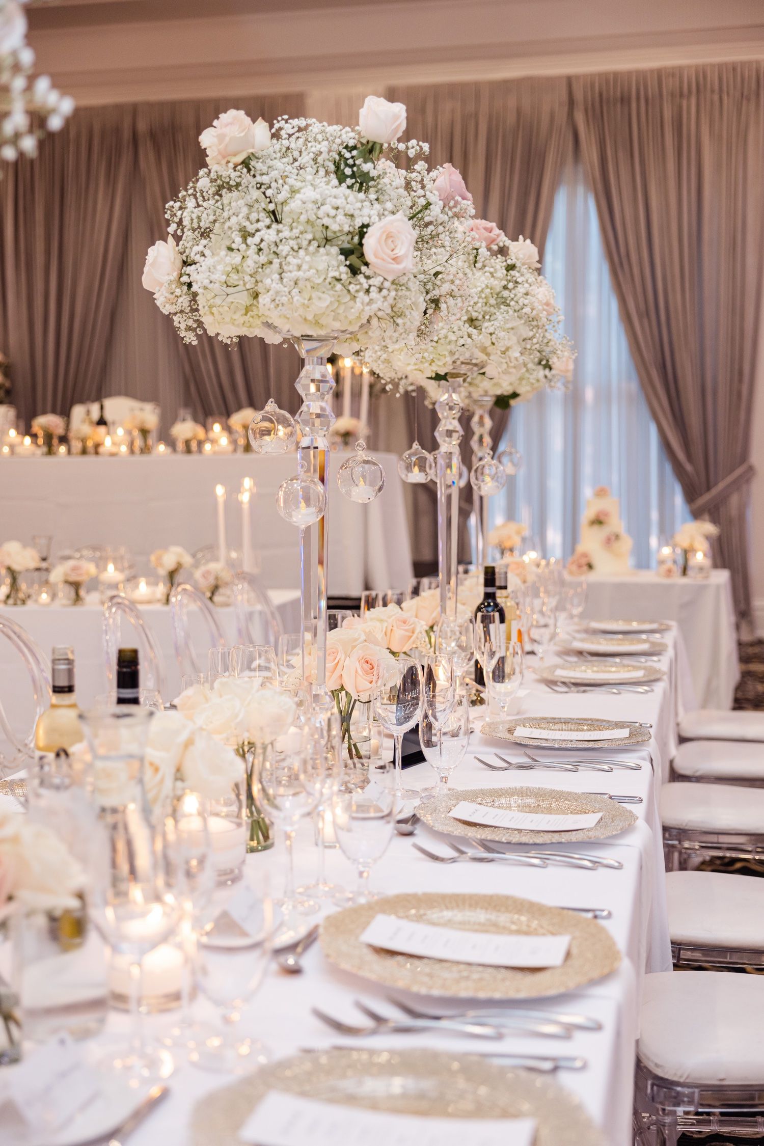 Elegant white wedding reception table with tall floral arrangements and gold charger plates.