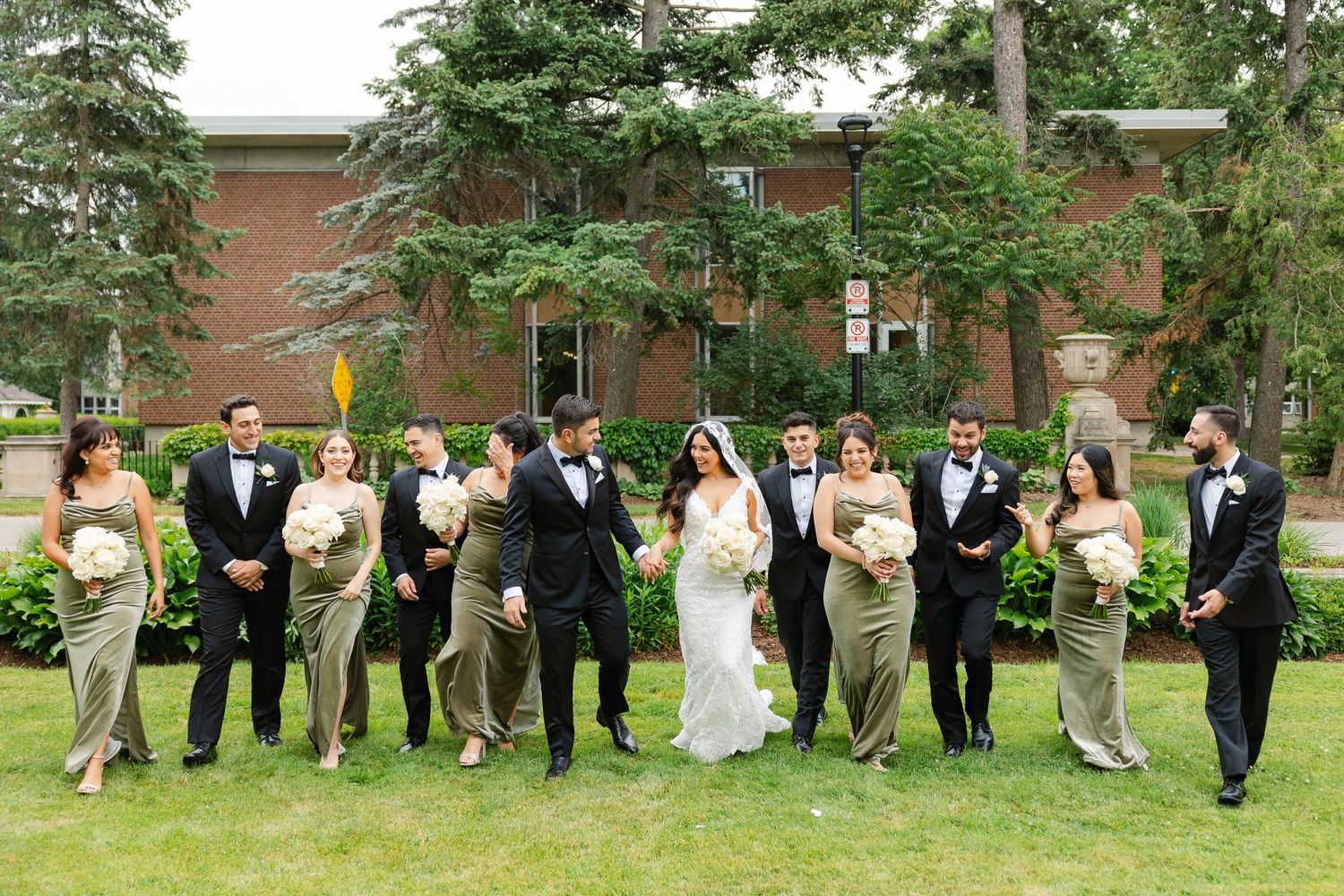 Fun outdoor portrait of wedding party striking playful poses on grass.