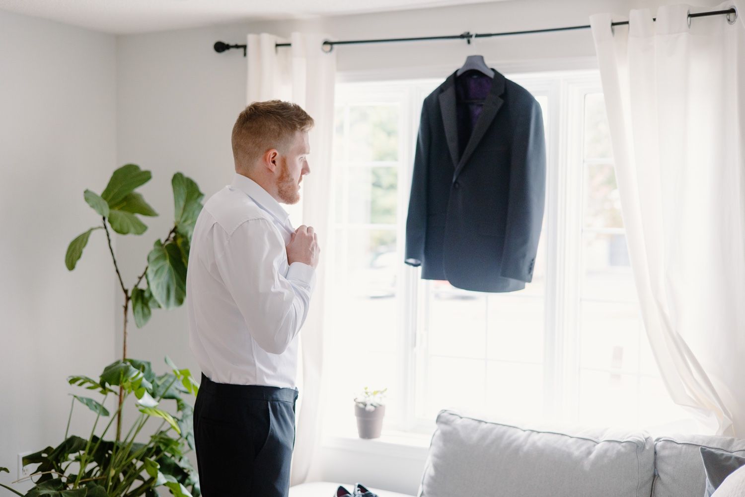 Getting ready scene with navy suit jacket hanging by window and indoor plant.