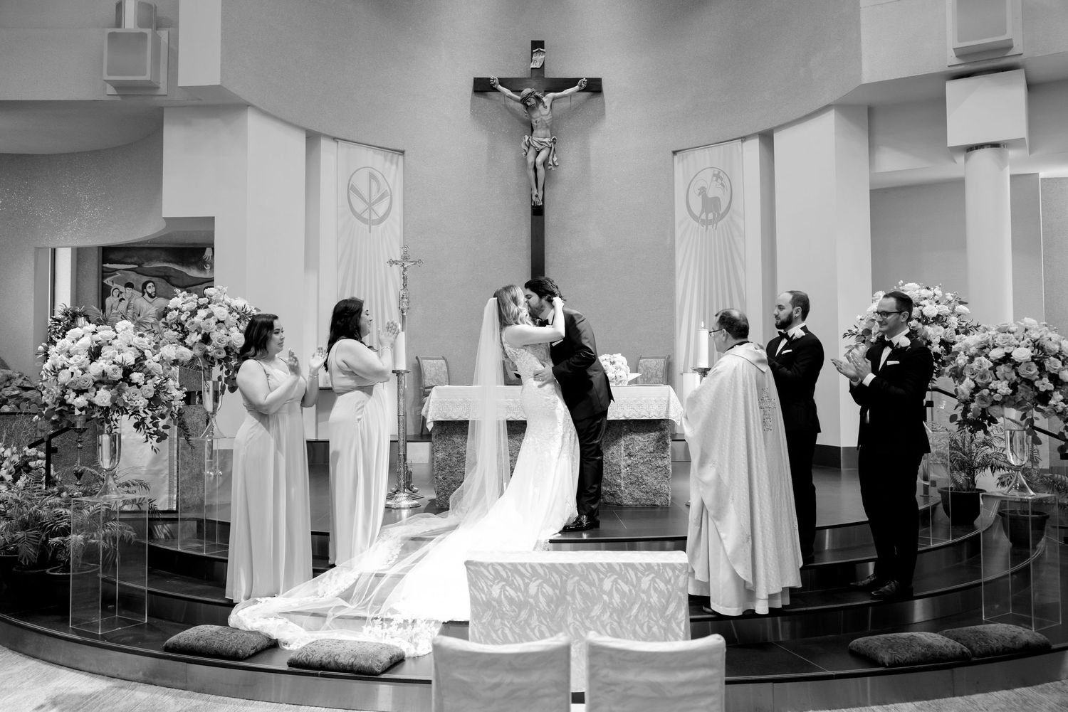Black and white photo of wedding ceremony with floral arrangements framing church altar.