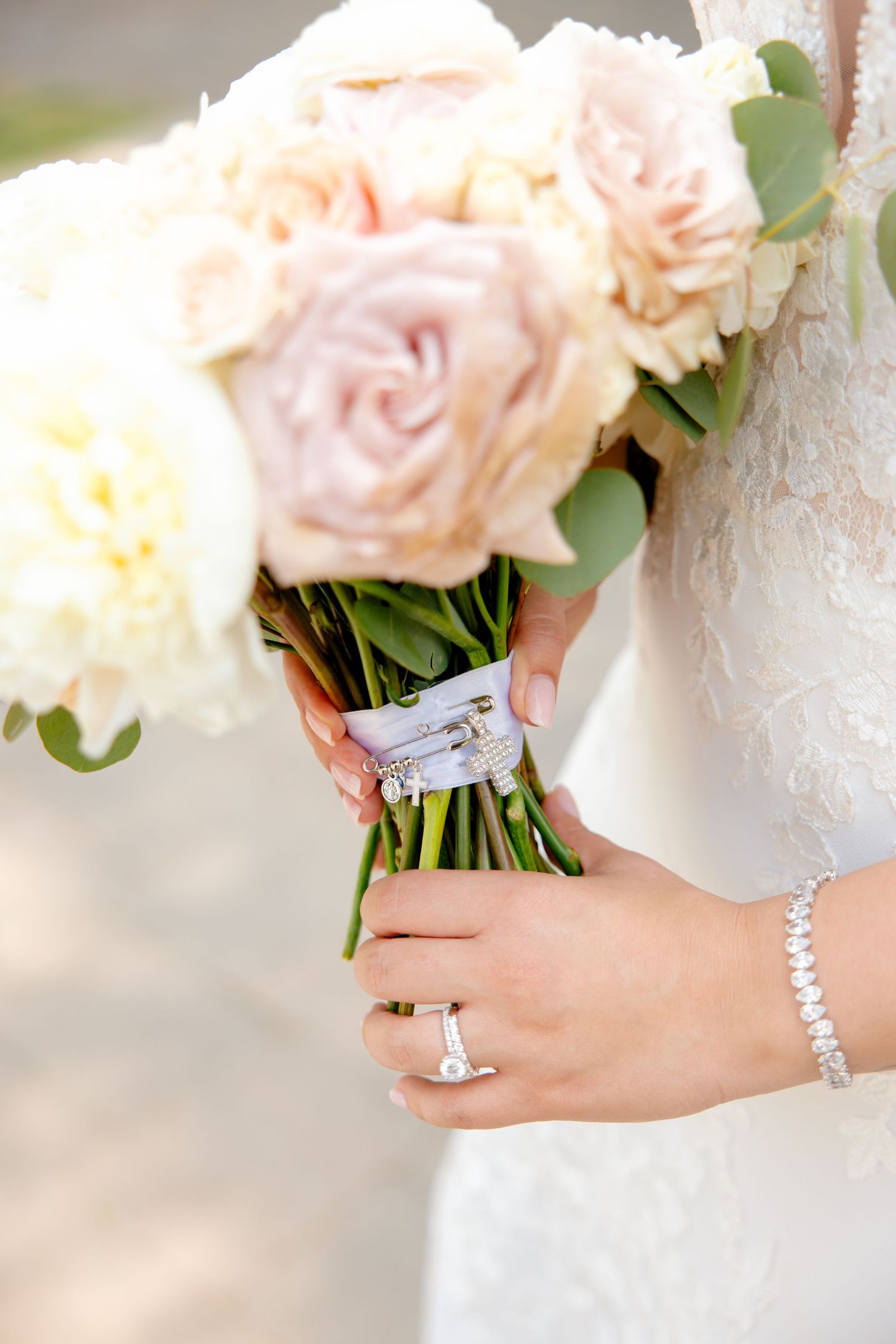 Wedding bouquet of blush roses wrapped in ribbon held by bride wearing jewelry.