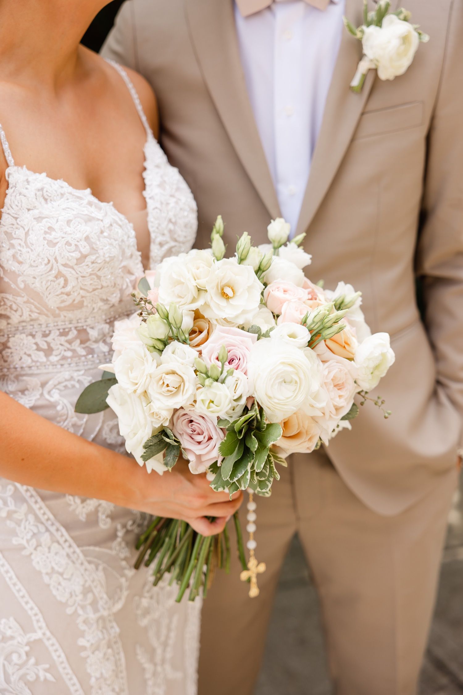 Elegant white and blush wedding bouquet showcased against tan suit and white lace dress details.