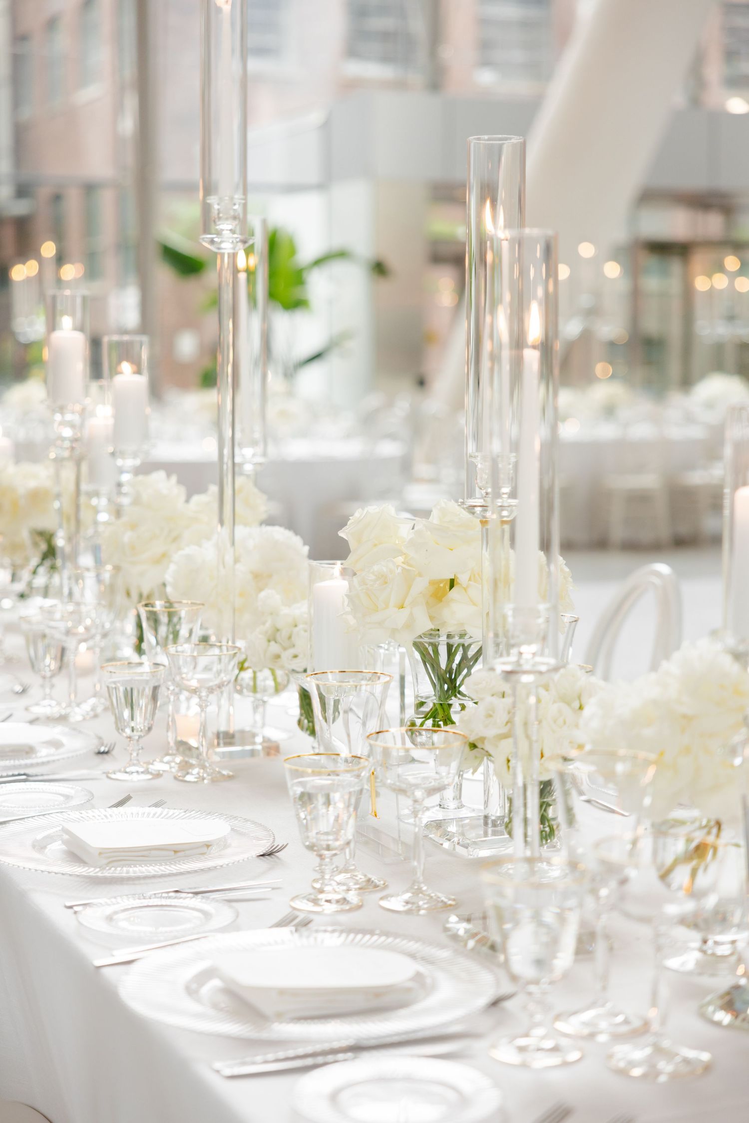 Luxurious white tablescape with crystal stemware, pillar candles, and white roses in glass vases.