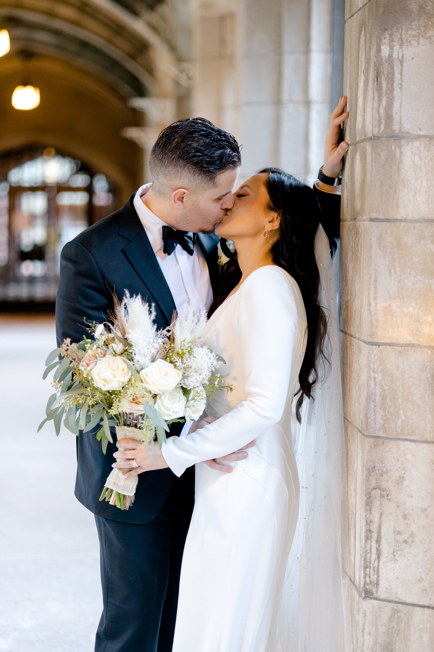 An elegant wedding portrait in a stone hallway with a bride holding a white and green bouquet.