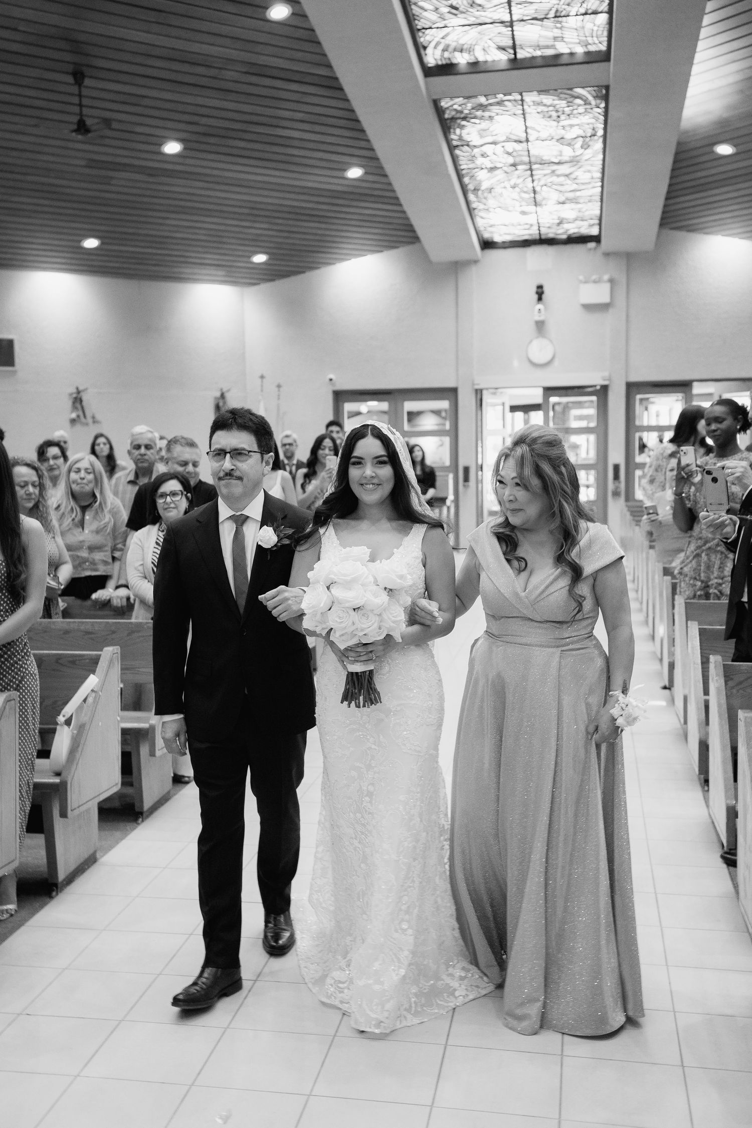 Black and white wedding processional photo in modern church with elegant lighting.
