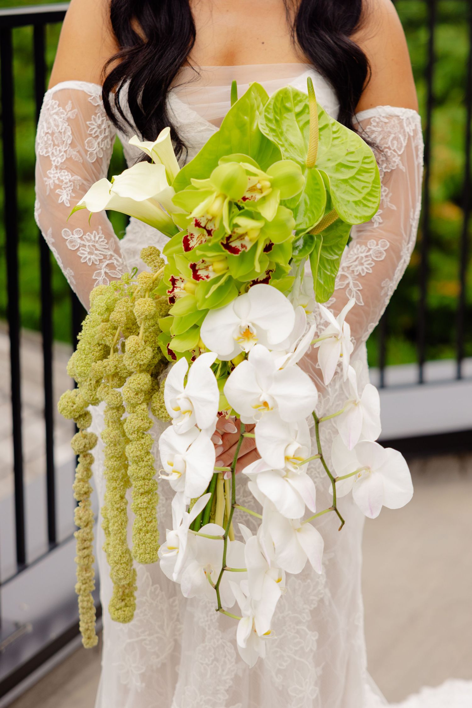 Elegant white orchid and green amaranthus wedding bouquet held against a white lace wedding dress.
