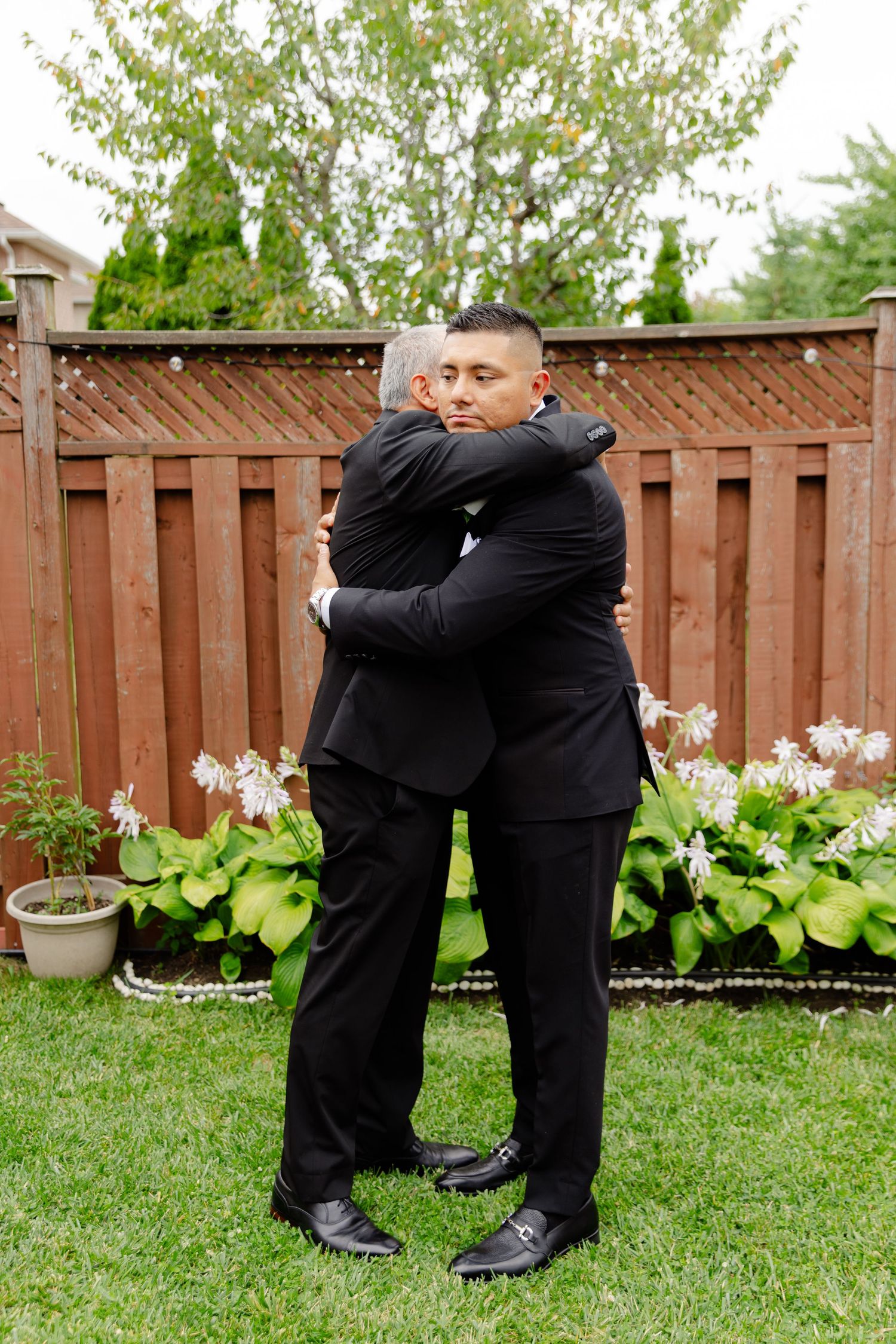 Wedding party members share playful embraces in a backyard garden setting.
