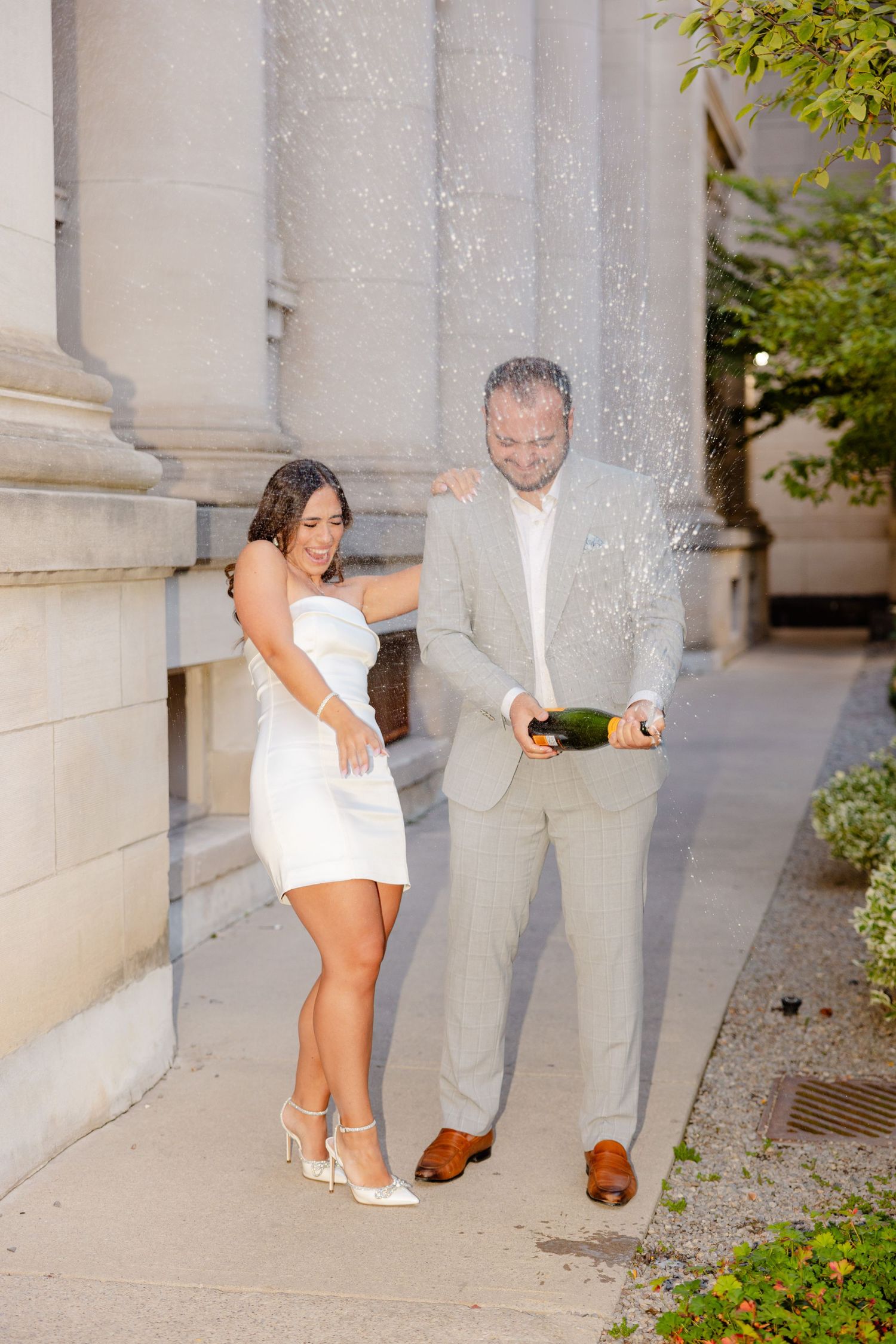 Champagne spray celebration moment captured against classical architecture background.