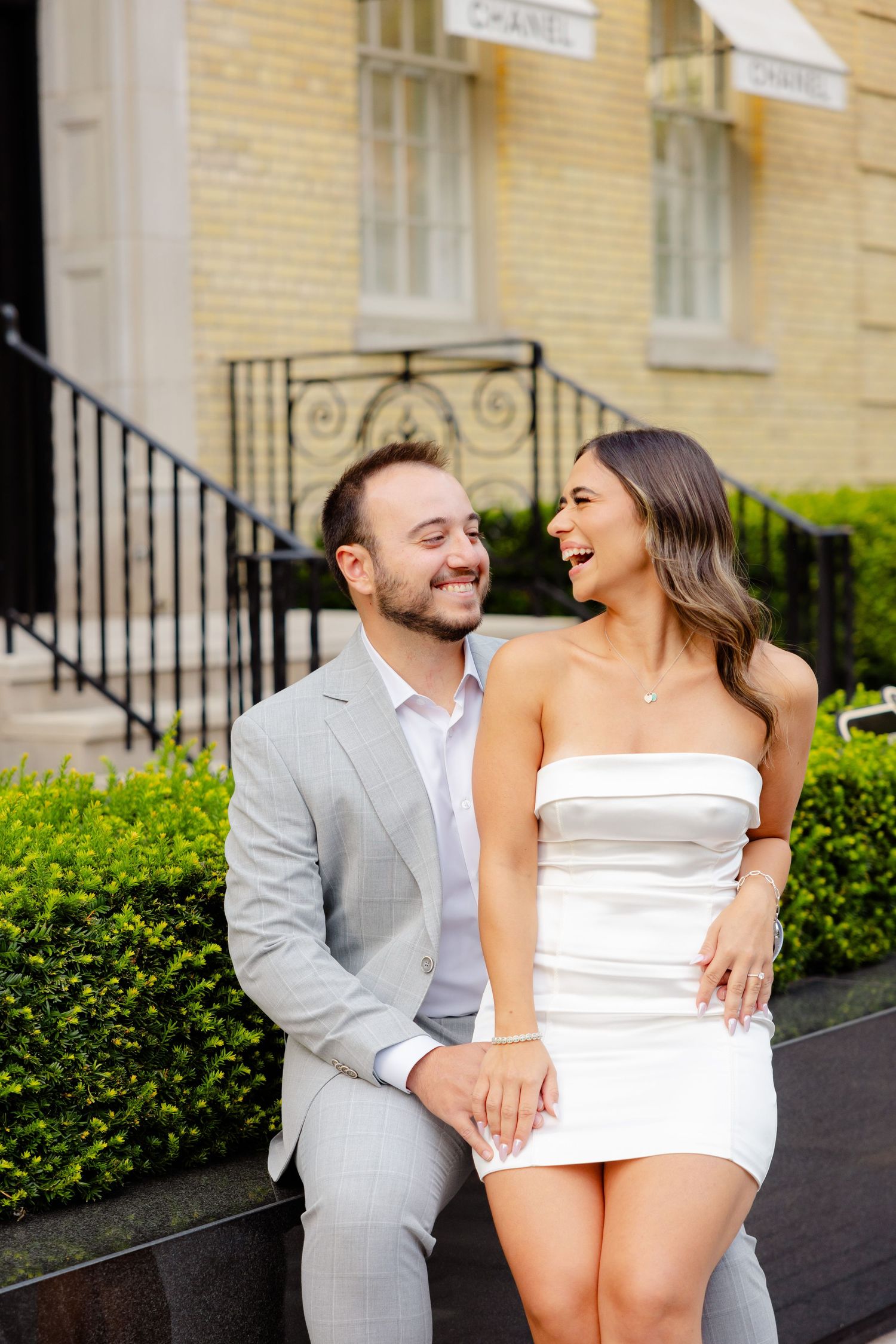Joyful moment captured between couple in coordinating formal wear outside luxury store.