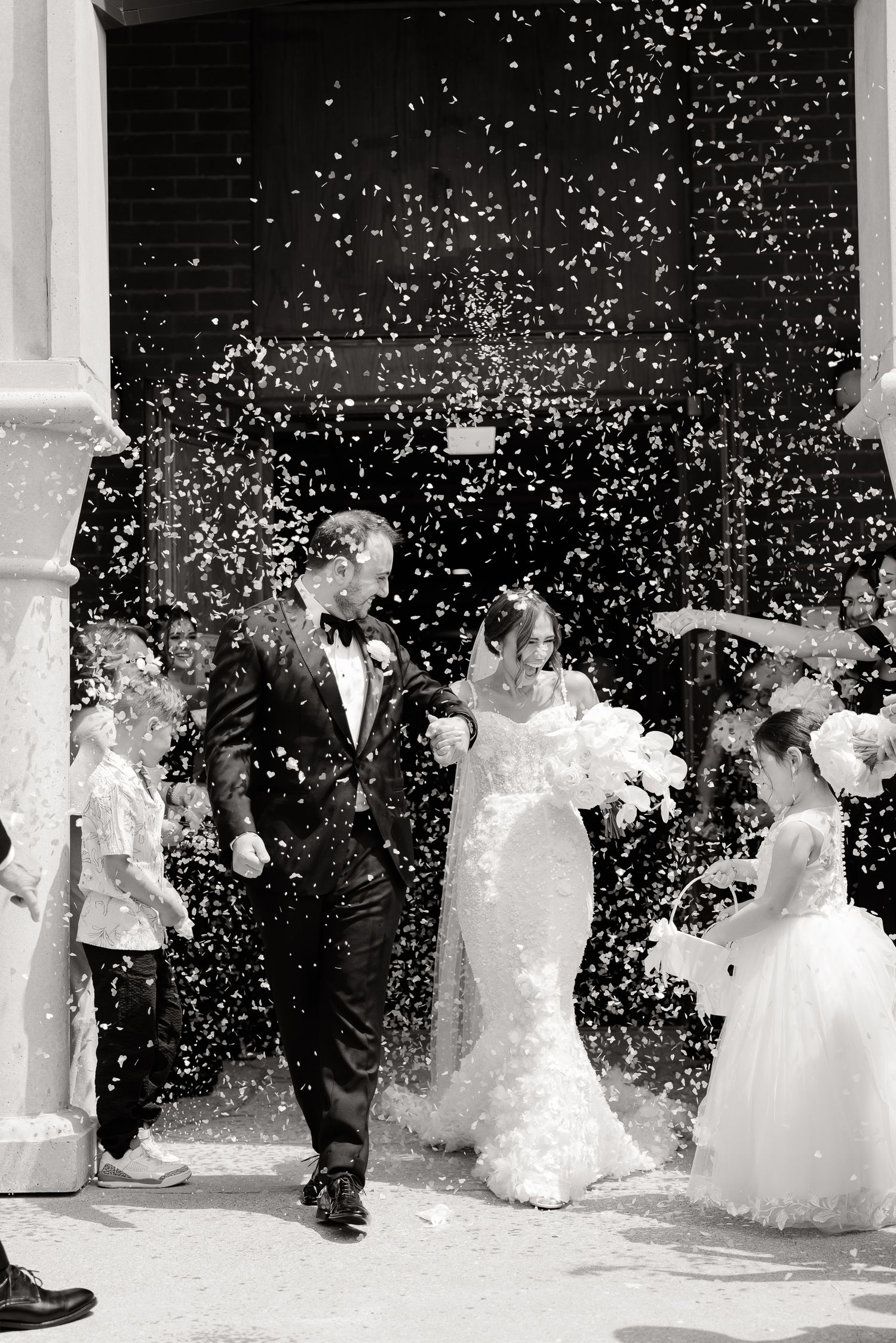 A bride and groom exit their wedding ceremony as guests shower them with rice confetti in a joyful celebration.