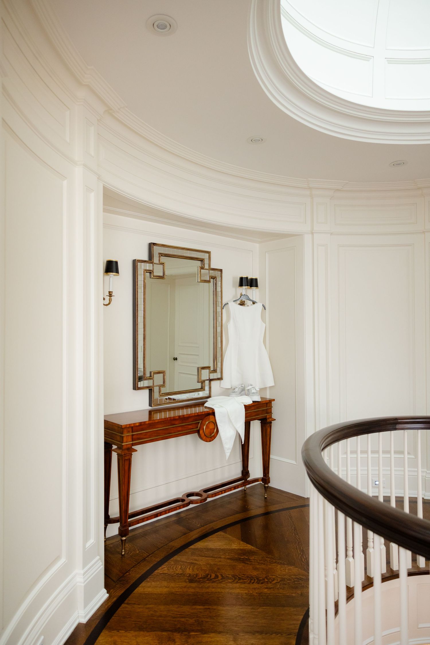 Curved staircase hallway with gold-framed mirror and wedding dress displayed on wooden console table.