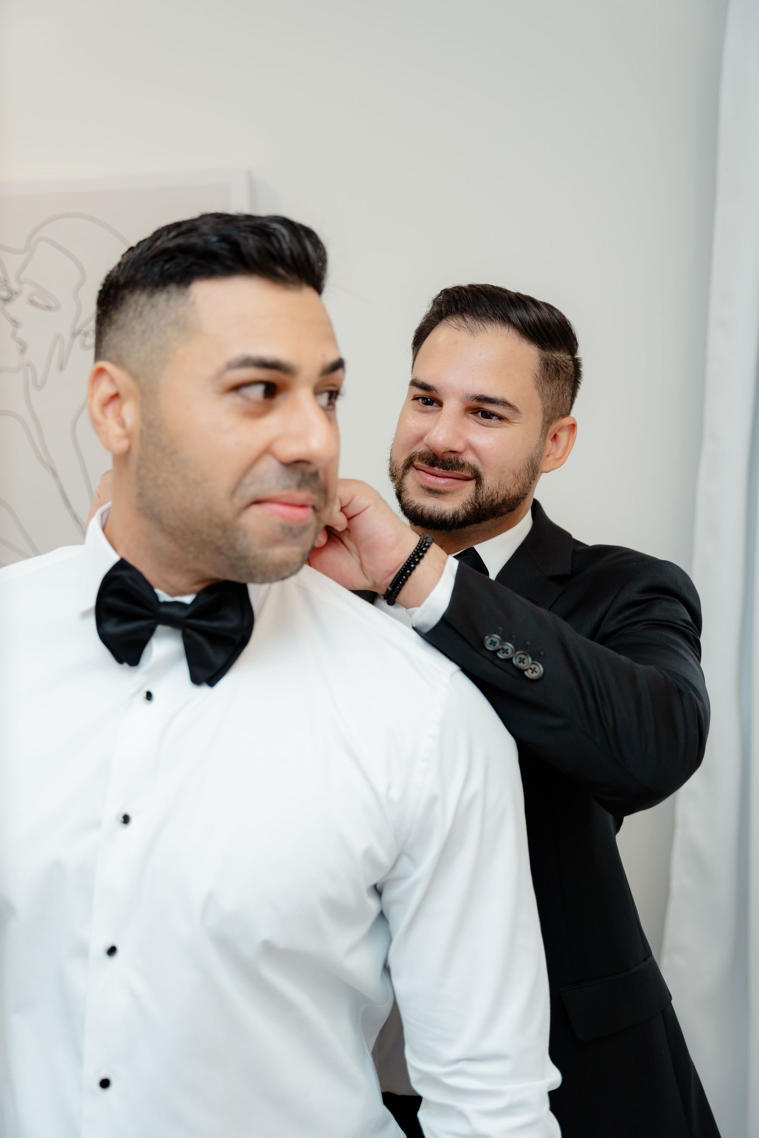 Wedding party members helping with formal attire adjustments in bright room.