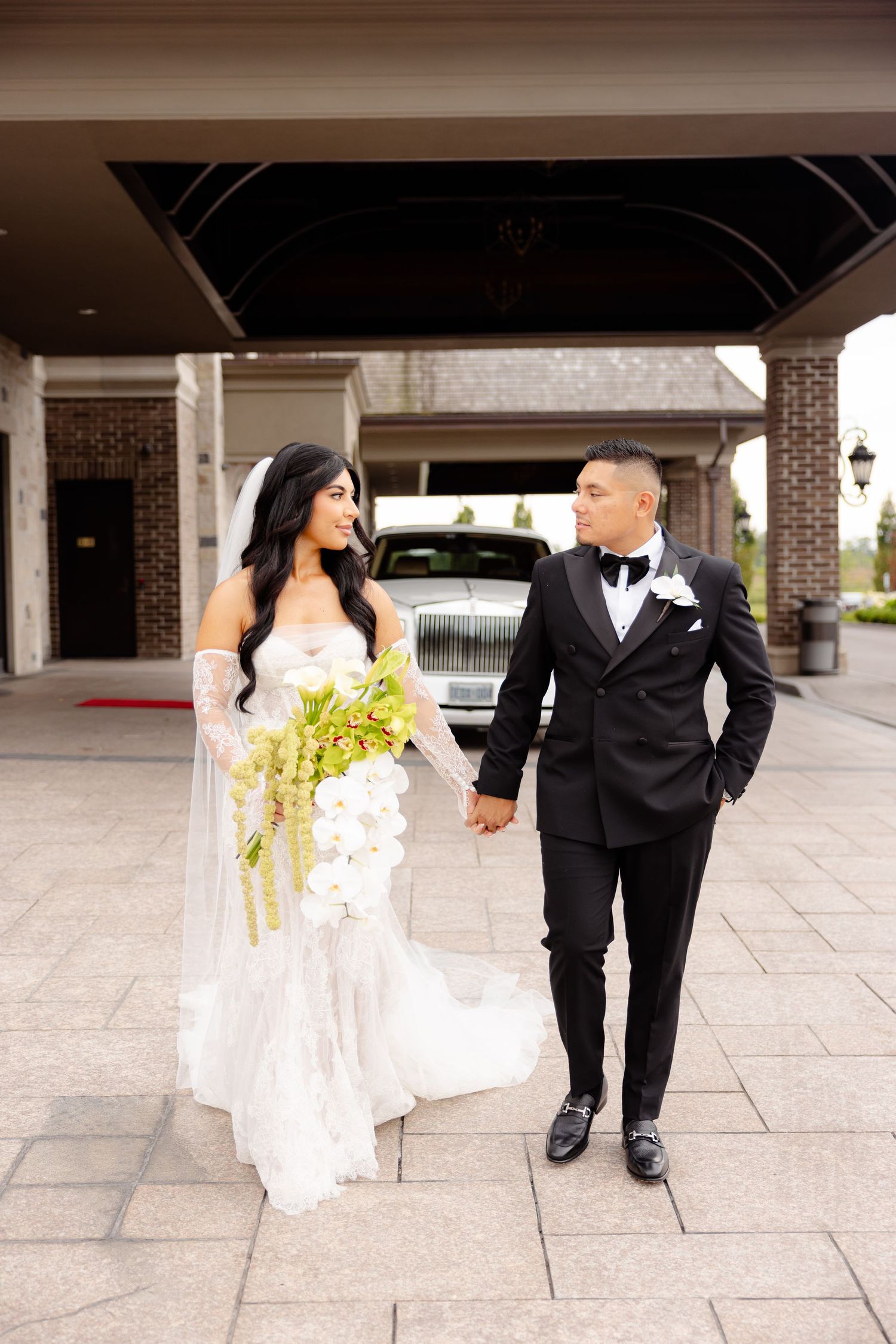 Wedding couple holding hands and walking together on a stone paved courtyard in black and white formal attire.