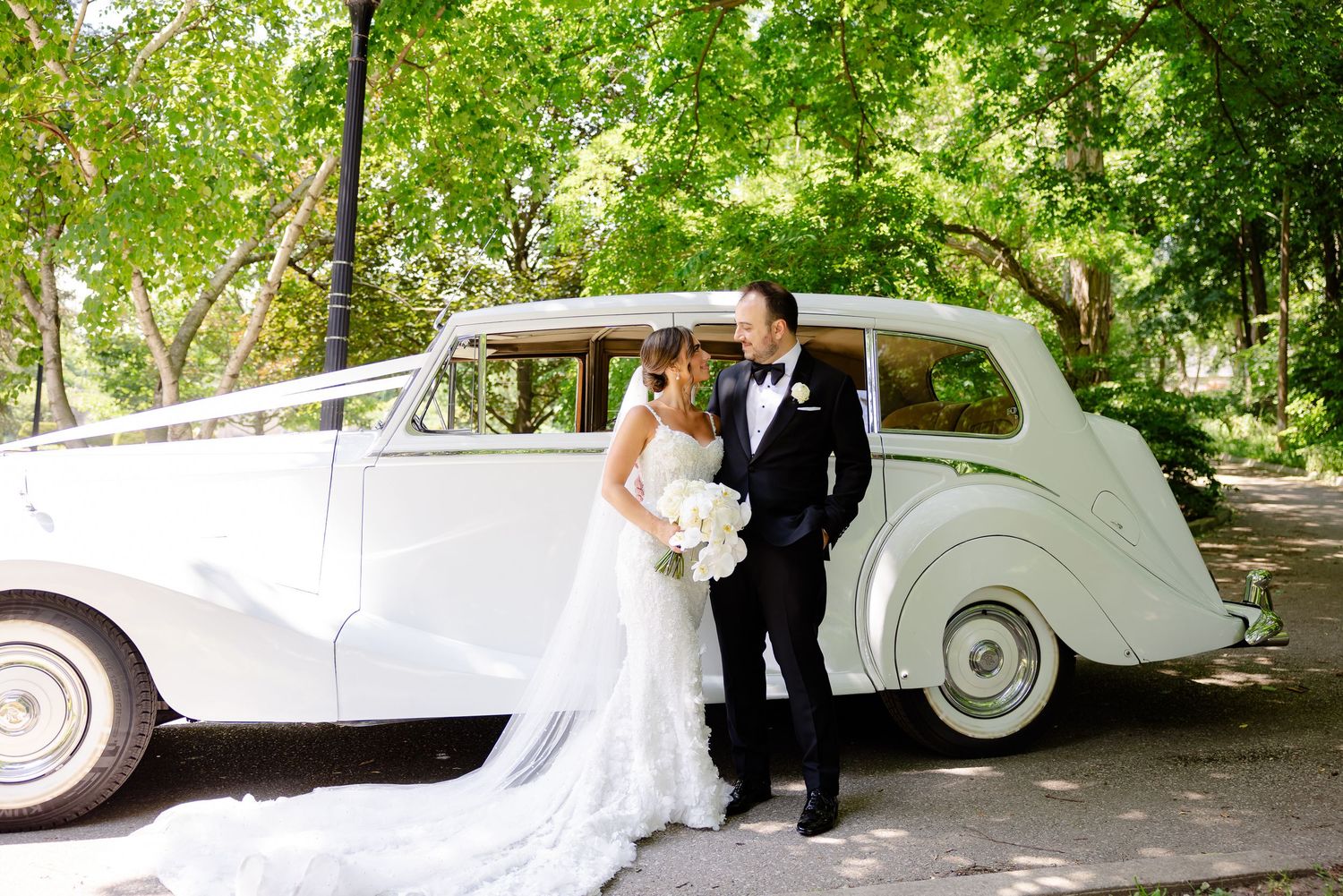 A classic white vintage Rolls Royce provides an elegant backdrop for a couple in formal wedding attire.
