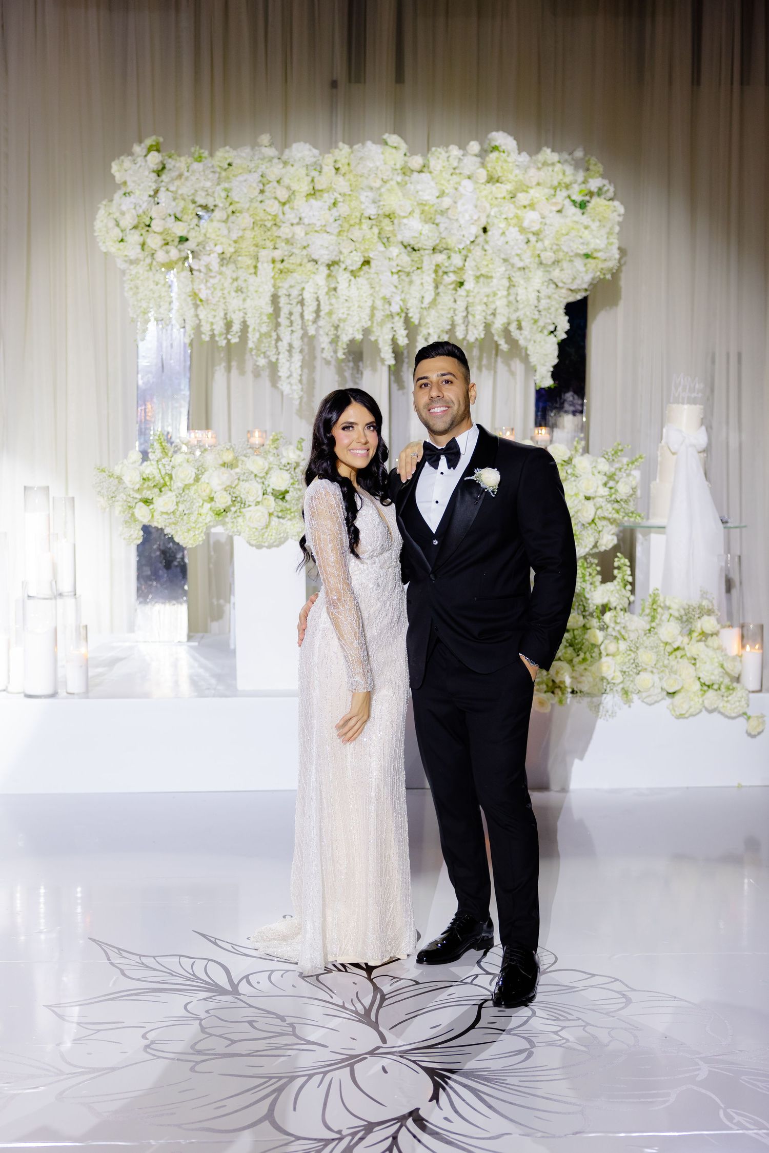 Elegant wedding portrait with couple standing beneath a cascading white floral installation.