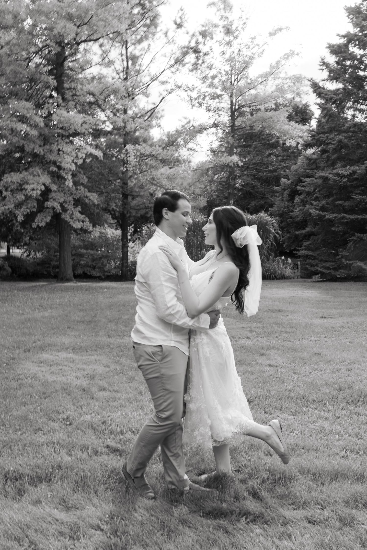 A playful black and white photo of newlyweds dancing in a garden setting.