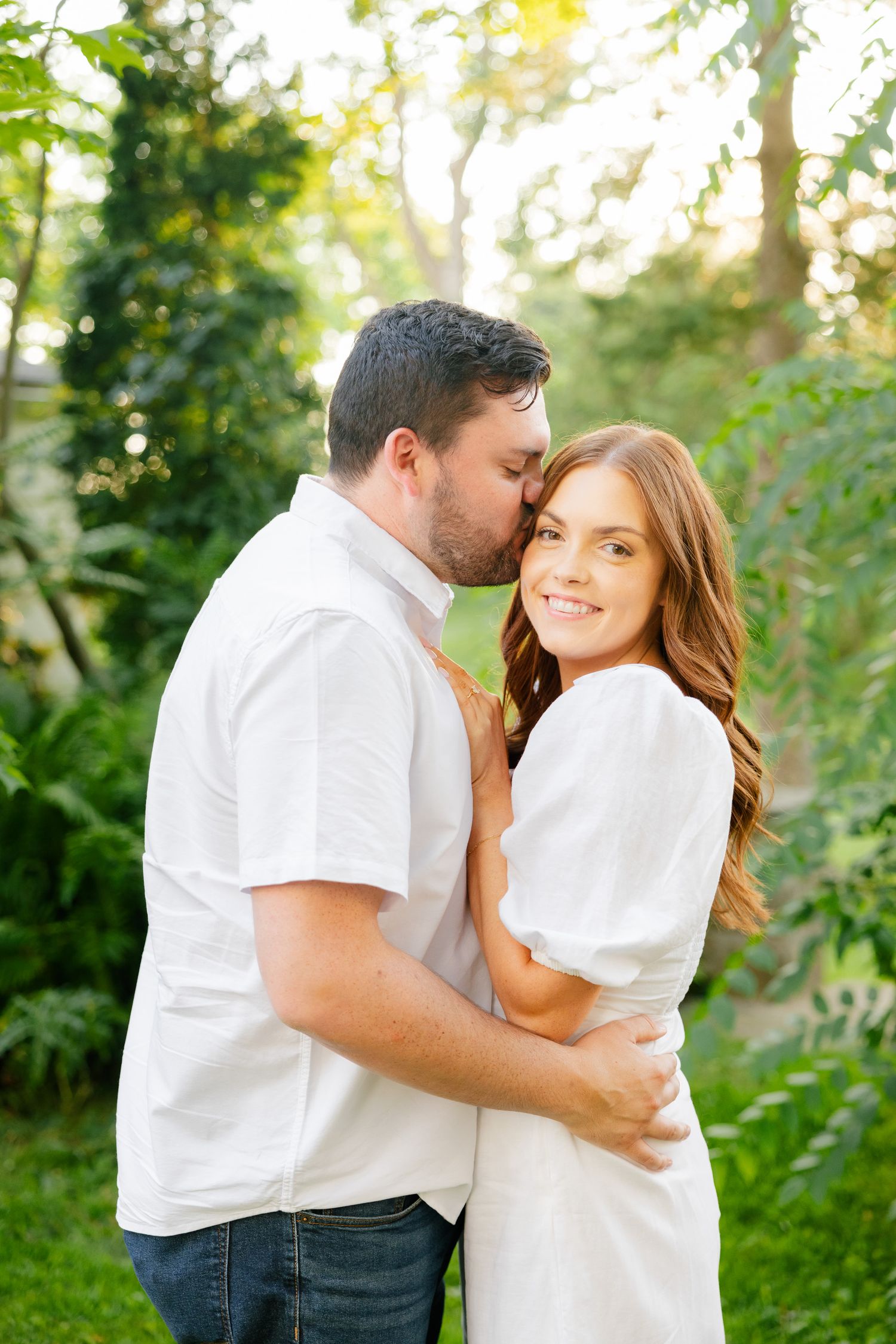 A tender moment between a couple wearing white as they share an intimate embrace outdoors.